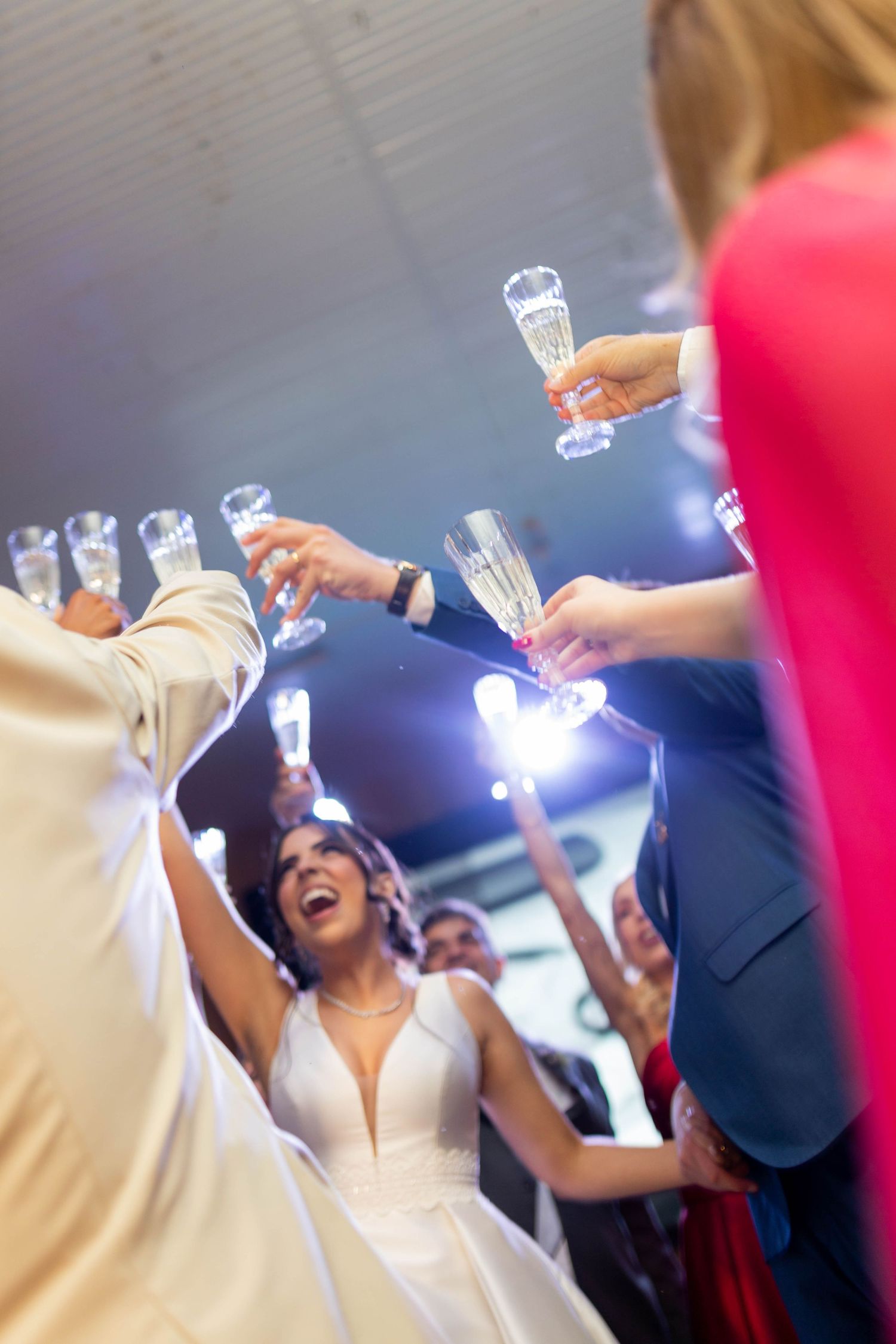Bride laughing joyfully as wedding guests raise champagne glasses in a celebratory toast at the reception.