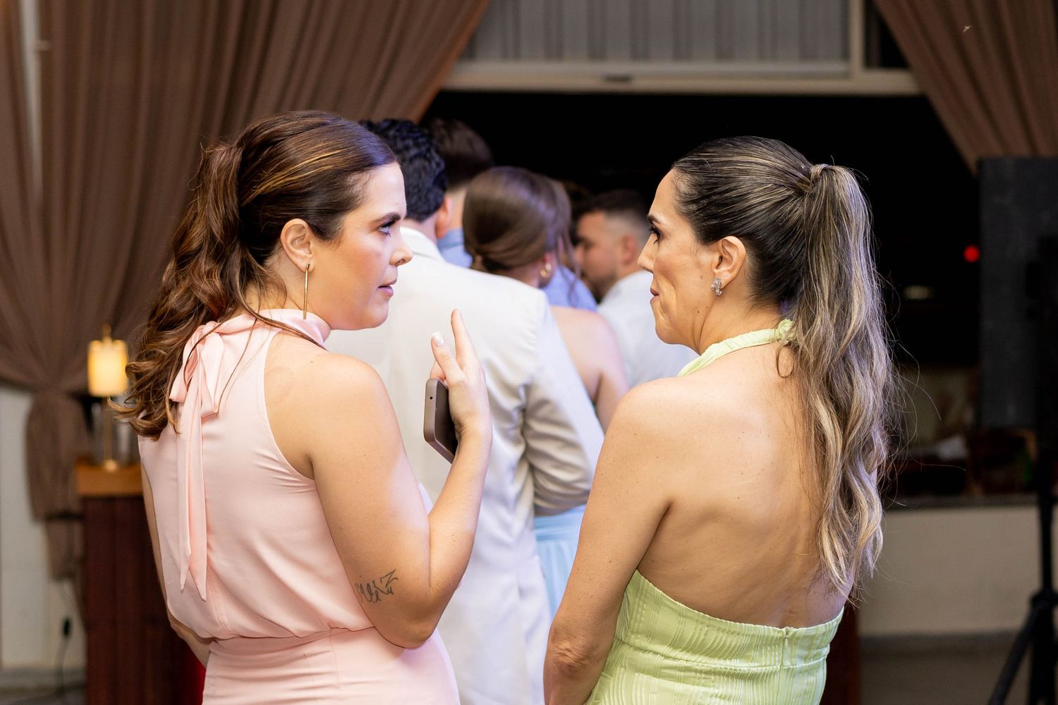 Two women in elegant dresses conversing and laughing at a wedding reception dance floor.