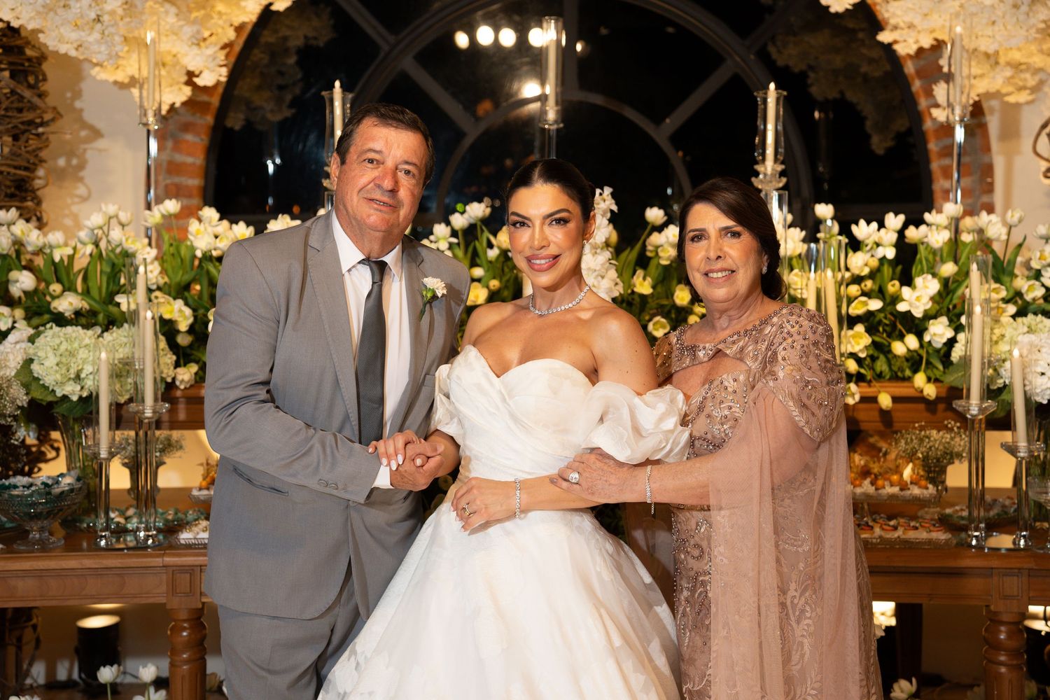 Bride in white ball gown poses with two guests at elegant floral wedding reception.