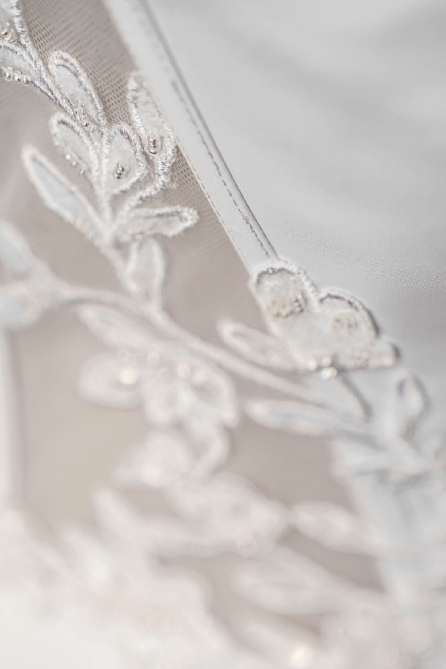 Close-up of delicate white floral lace embroidery with pearl beading on a bridal wedding veil or gown.