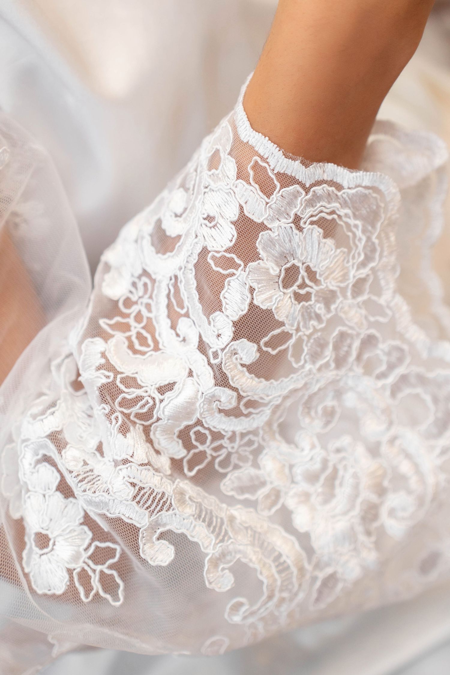 Close-up of an elegant white lace bridal glove with intricate floral embroidery on a wedding dress.