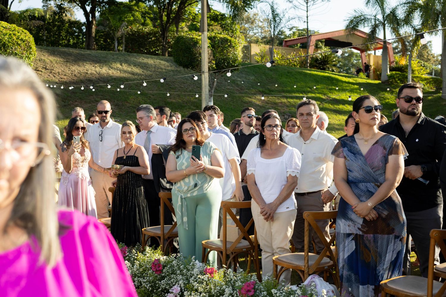 Guests standing outdoors at a garden wedding ceremony surrounded by lush greenery and floral arrangements.
