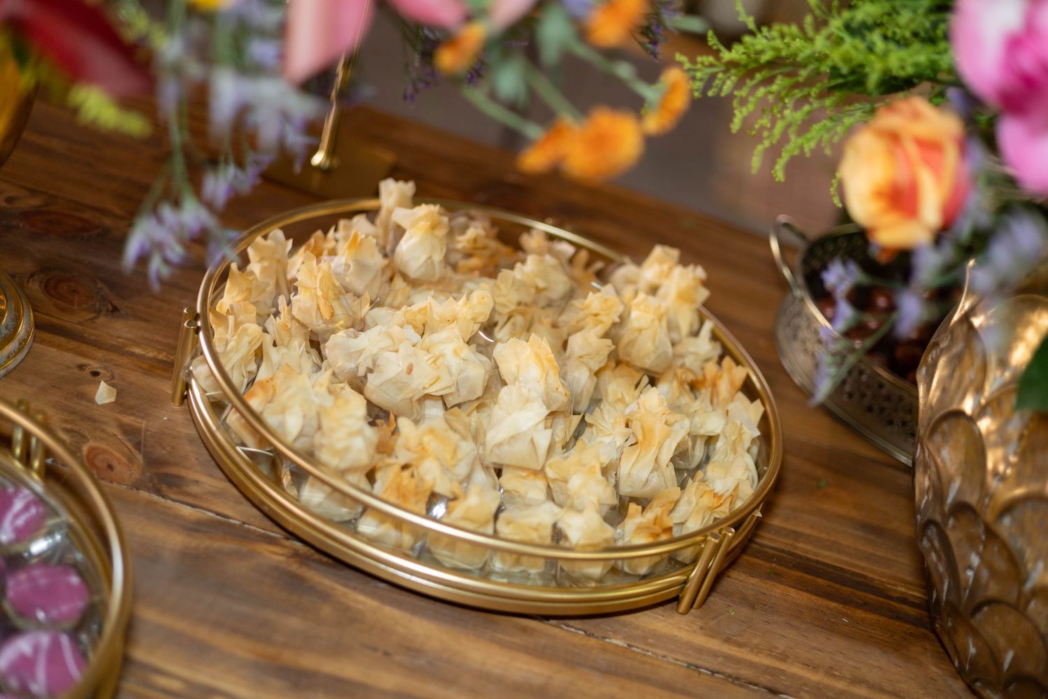 Gold tray filled with bite-sized cream puff pastries on a rustic wooden table with floral decorations.