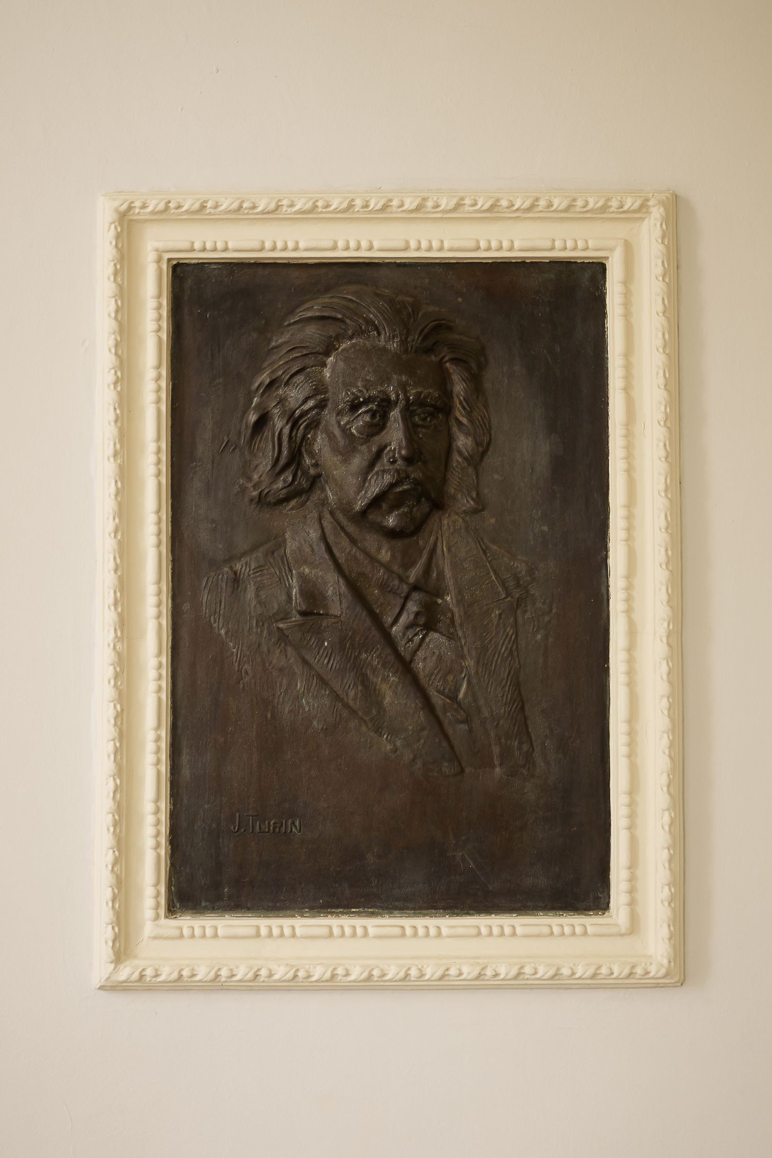 Bronze relief portrait plaque of a distinguished man in a white decorative frame mounted on a wall.