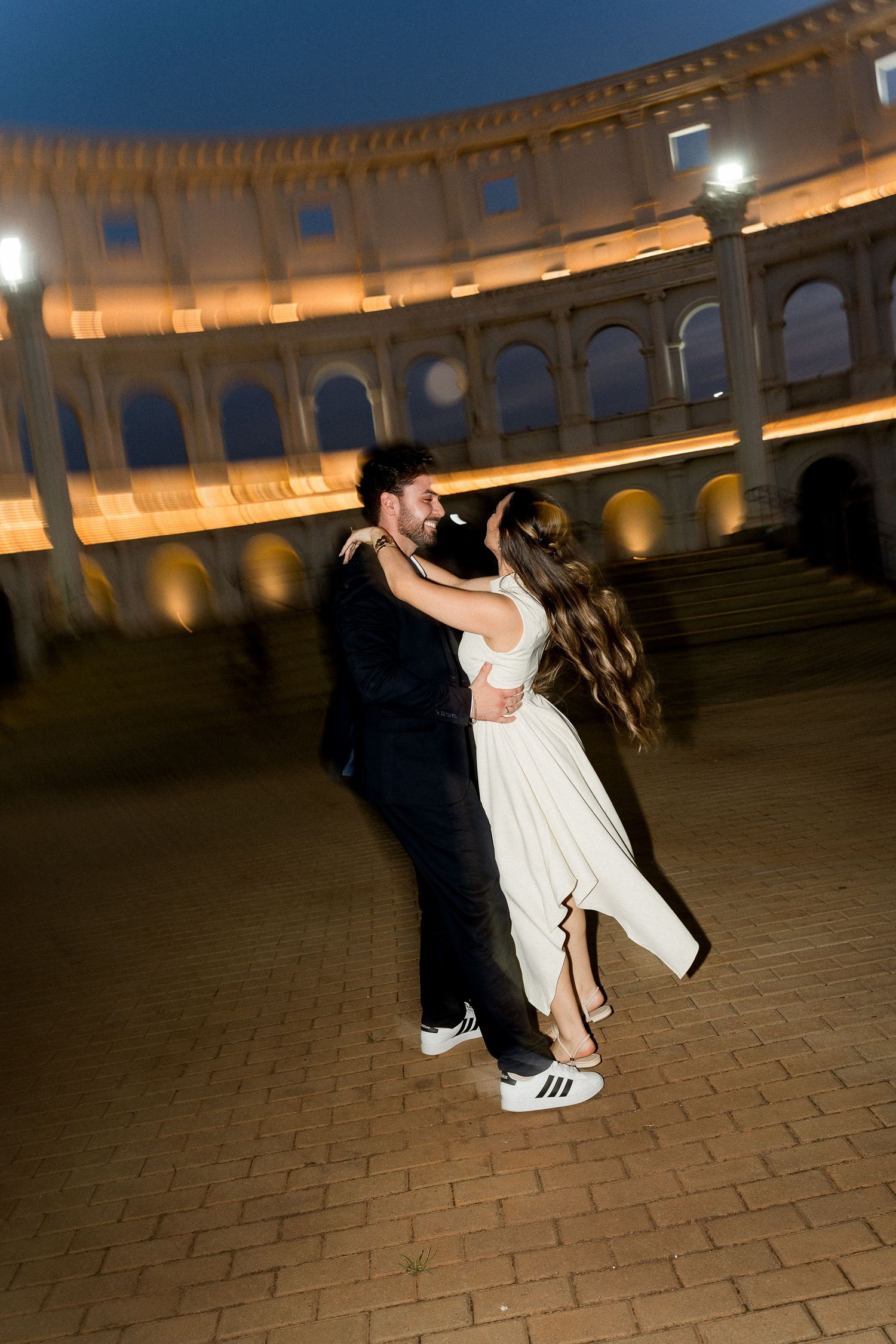 Couple dancing romantically at night inside the illuminated Colosseum in Rome, Italy.
