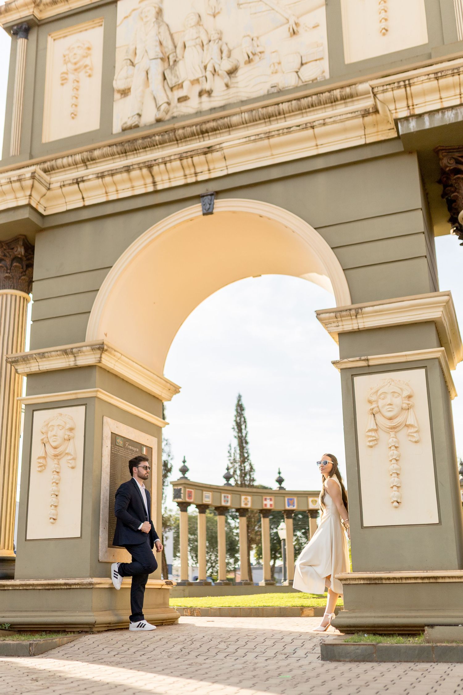 Elegant couple posing under a grand ornate arch with classical reliefs at a historic European venue.