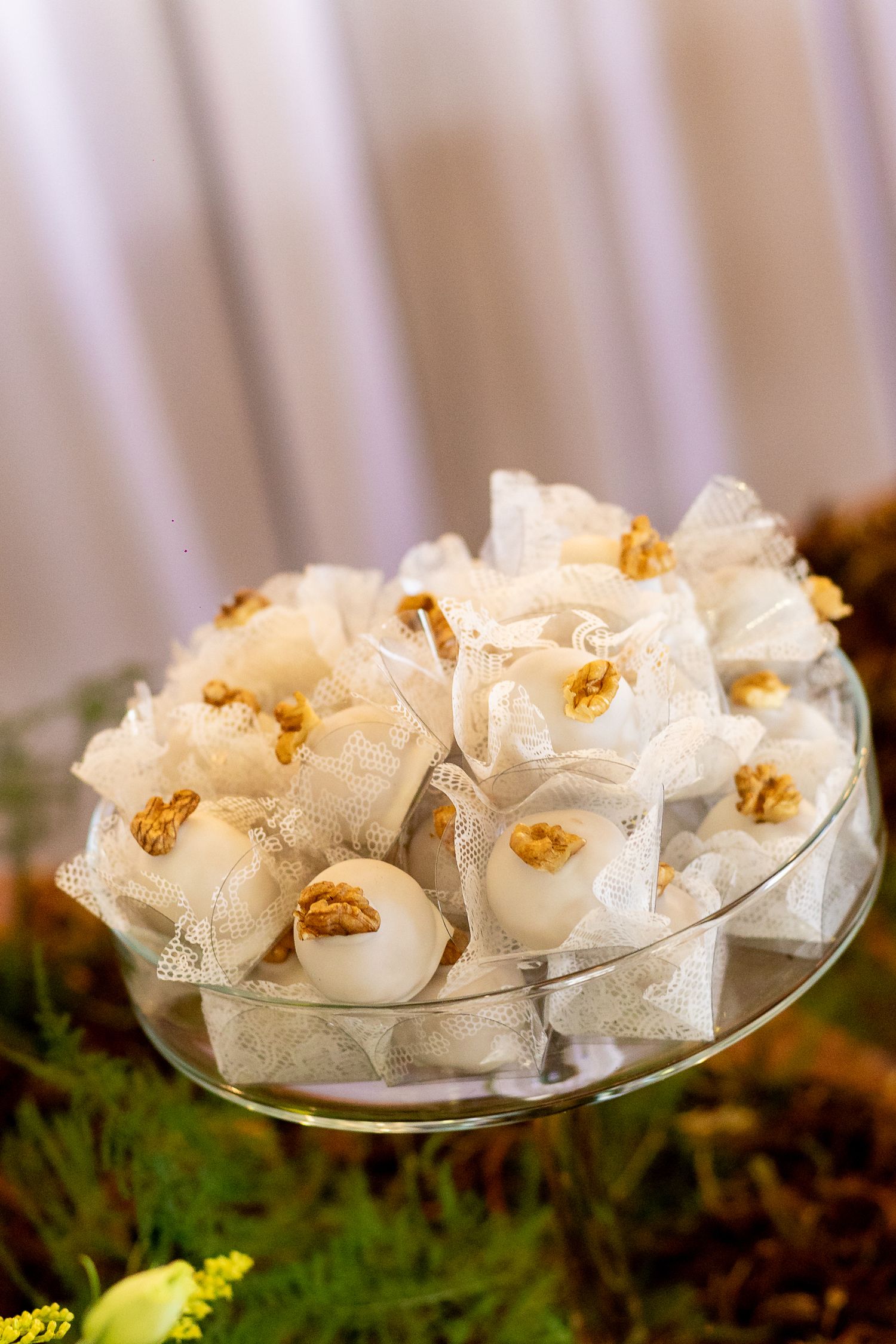 Elegant white lace-wrapped candies topped with walnuts displayed on a glass cake stand at a wedding reception.