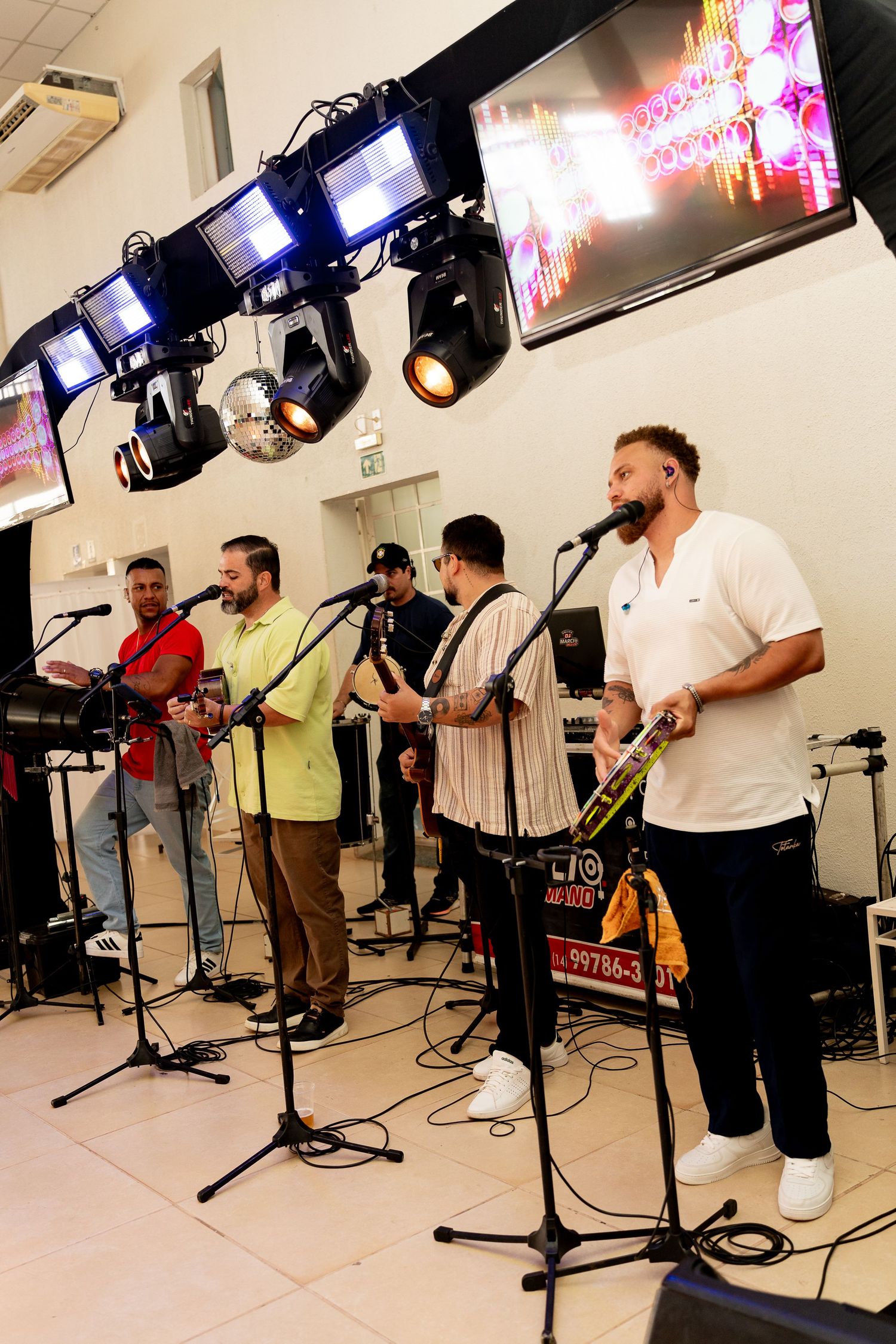 Live band performing on stage with microphones, stage lighting, and screens in a modern indoor venue.