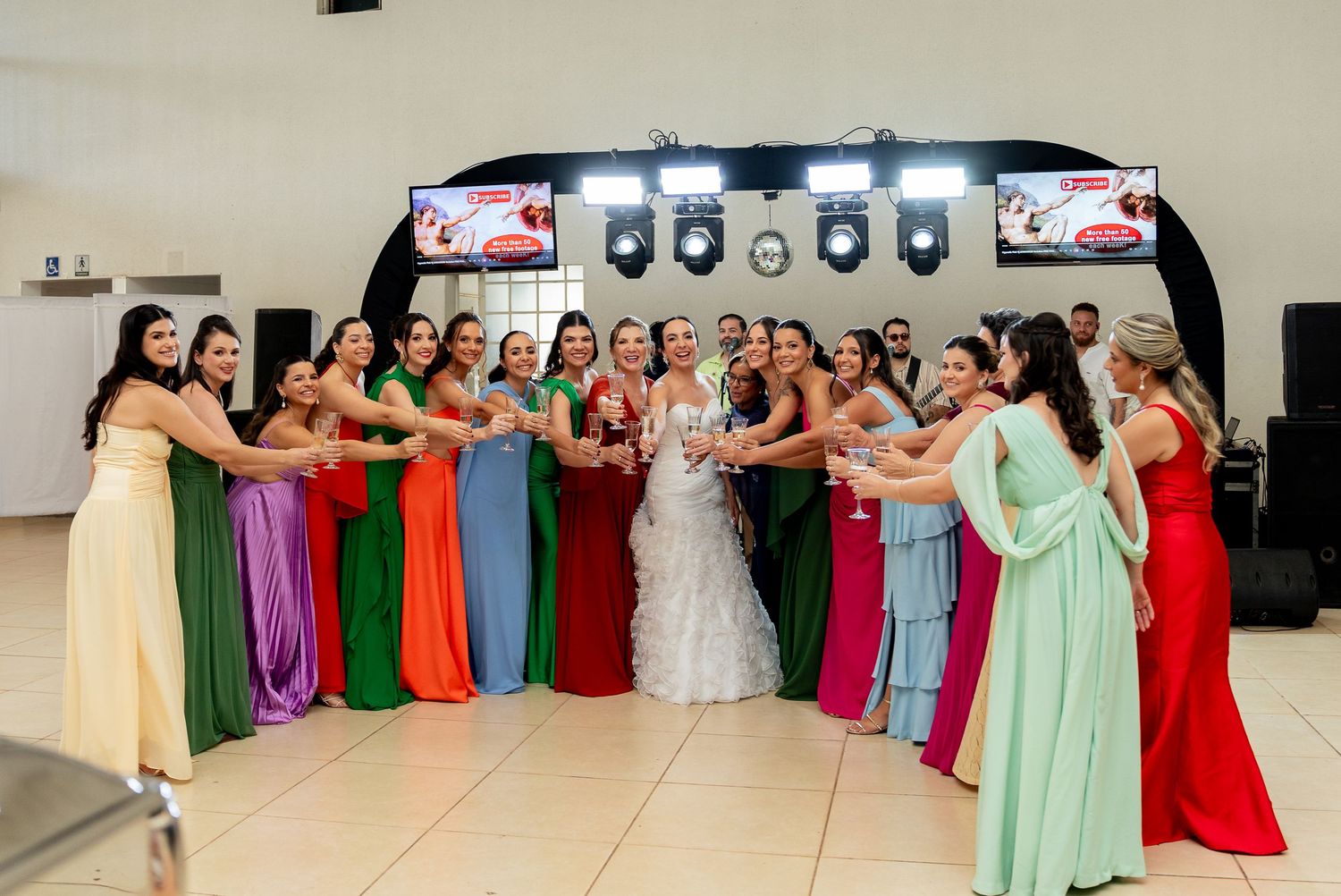 Bride surrounded by colorful bridesmaids in rainbow dresses toasting at a wedding reception venue.
