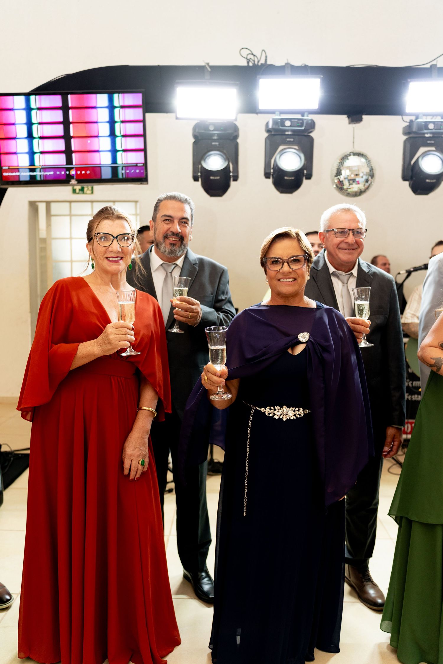 Elegantly dressed guests toasting with champagne glasses at a formal evening event under stage lighting.