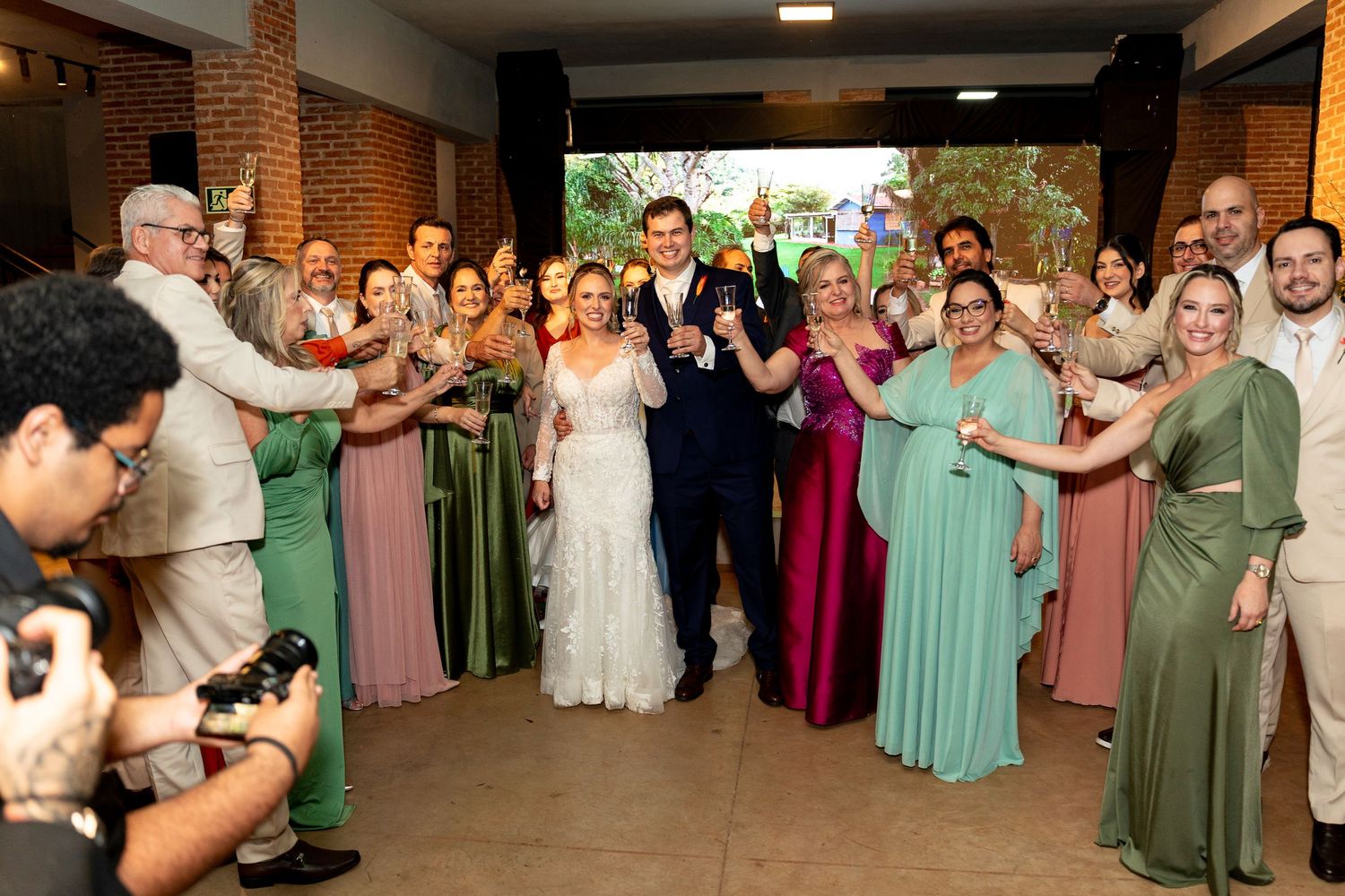 Bride and groom celebrate with wedding party in elegant venue, bridesmaids in green and pink gowns.