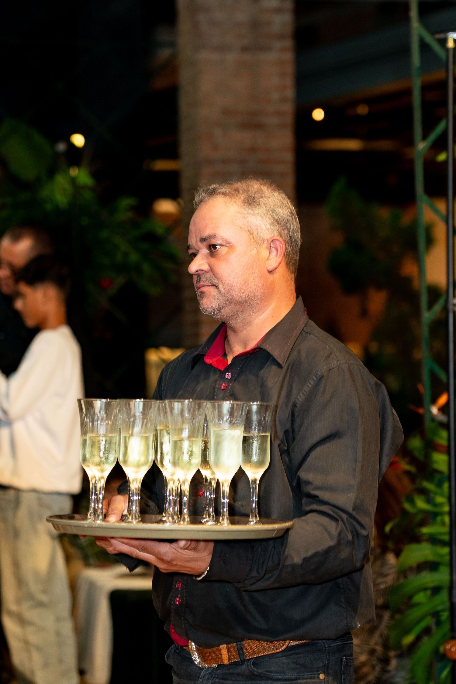 A waiter carries a tray of champagne glasses at an outdoor evening event.
