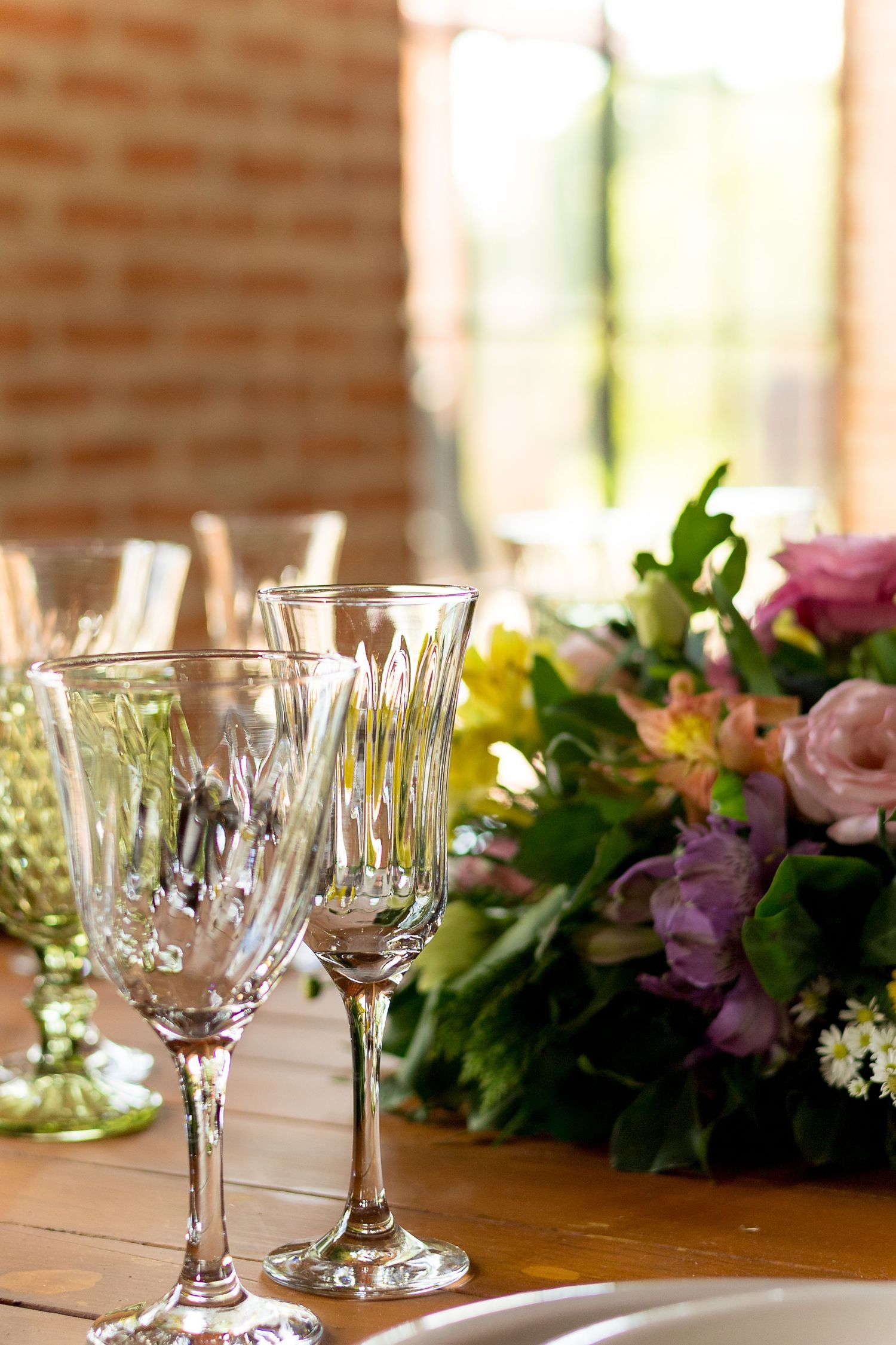 Crystal wine glasses on a wooden table with a colorful floral centerpiece at an elegant event.