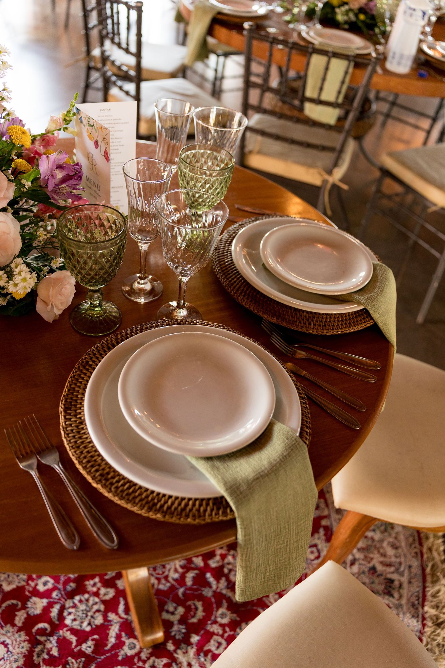 Elegant round wooden table set with white plates, green napkins, crystal glasses, and floral centerpiece for a formal dinner.