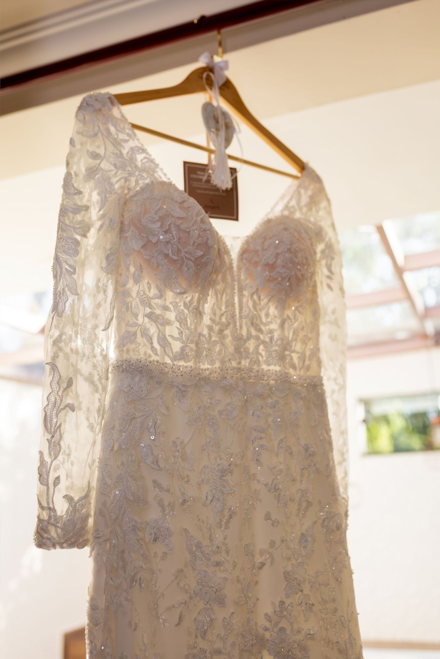 Elegant lace wedding dress with long sleeves and sweetheart neckline hanging on wooden hanger.