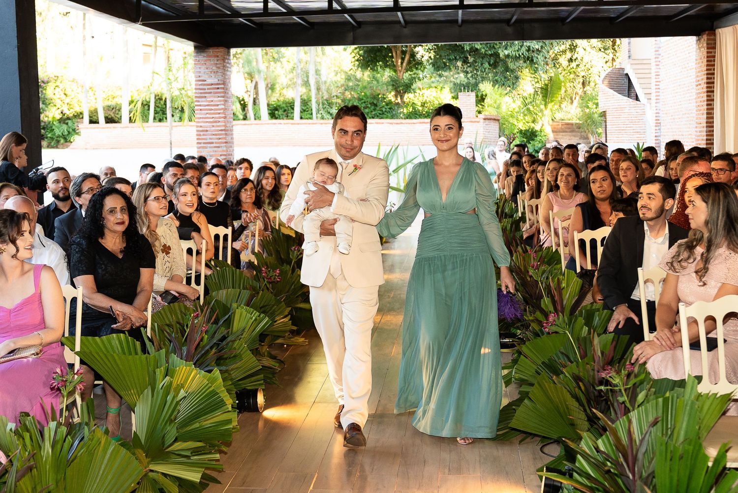 Elegant wedding ceremony procession with couple in teal gown and white suit walking down aisle.