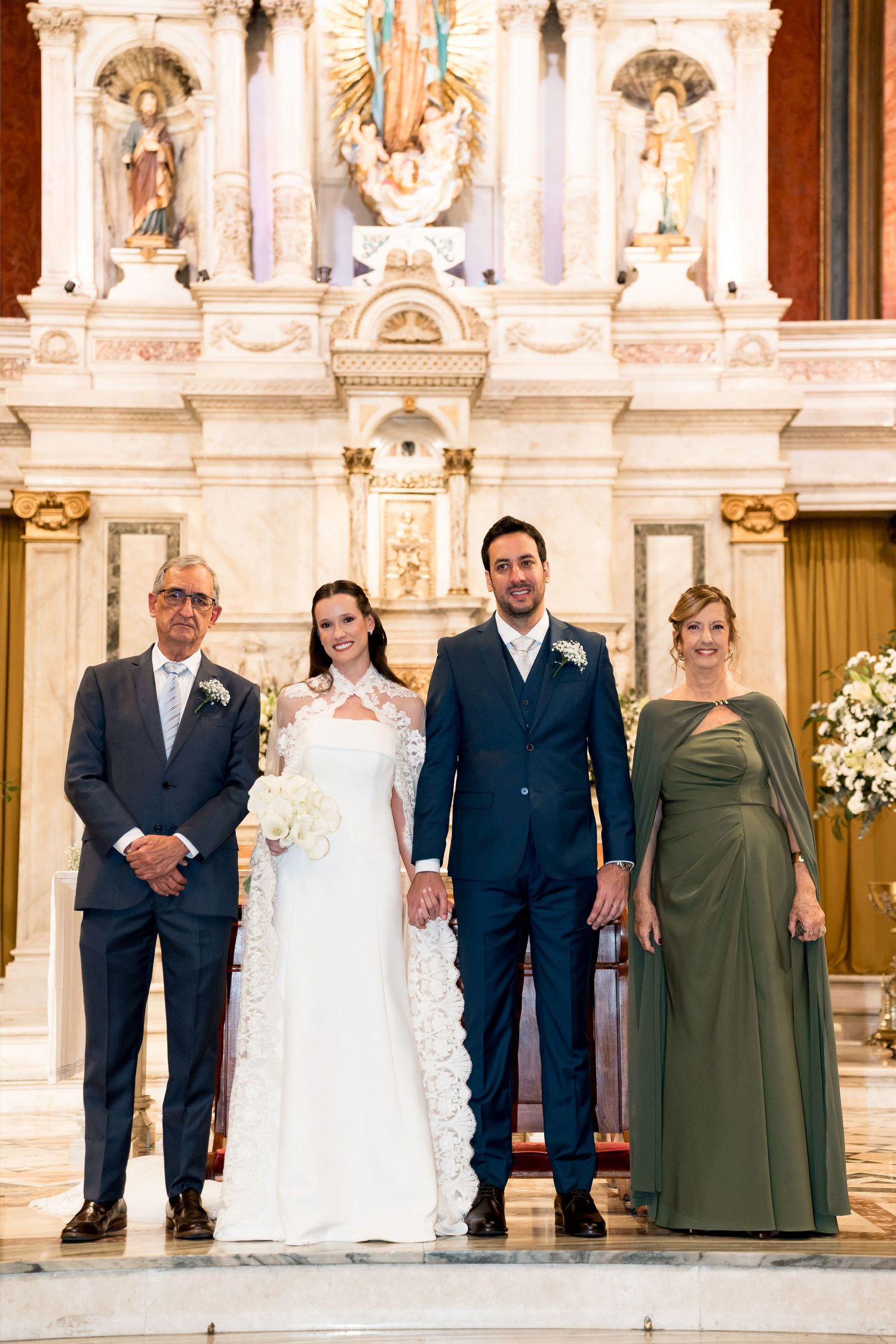 Bride and groom pose with family members at church altar during elegant wedding ceremony.
