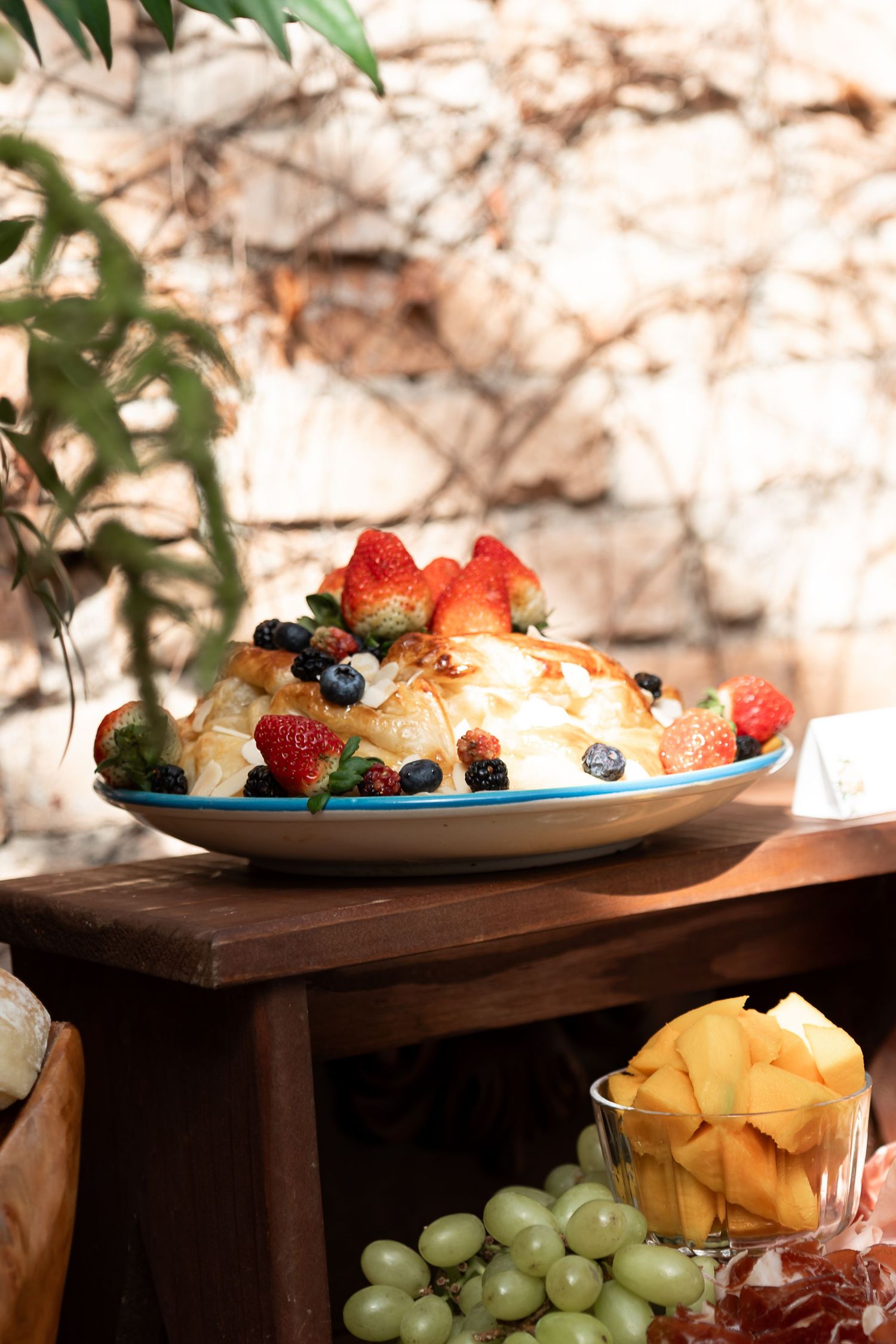 A elegant dessert platter topped with fresh strawberries and berries, drizzled with caramel, displayed on a wooden table.