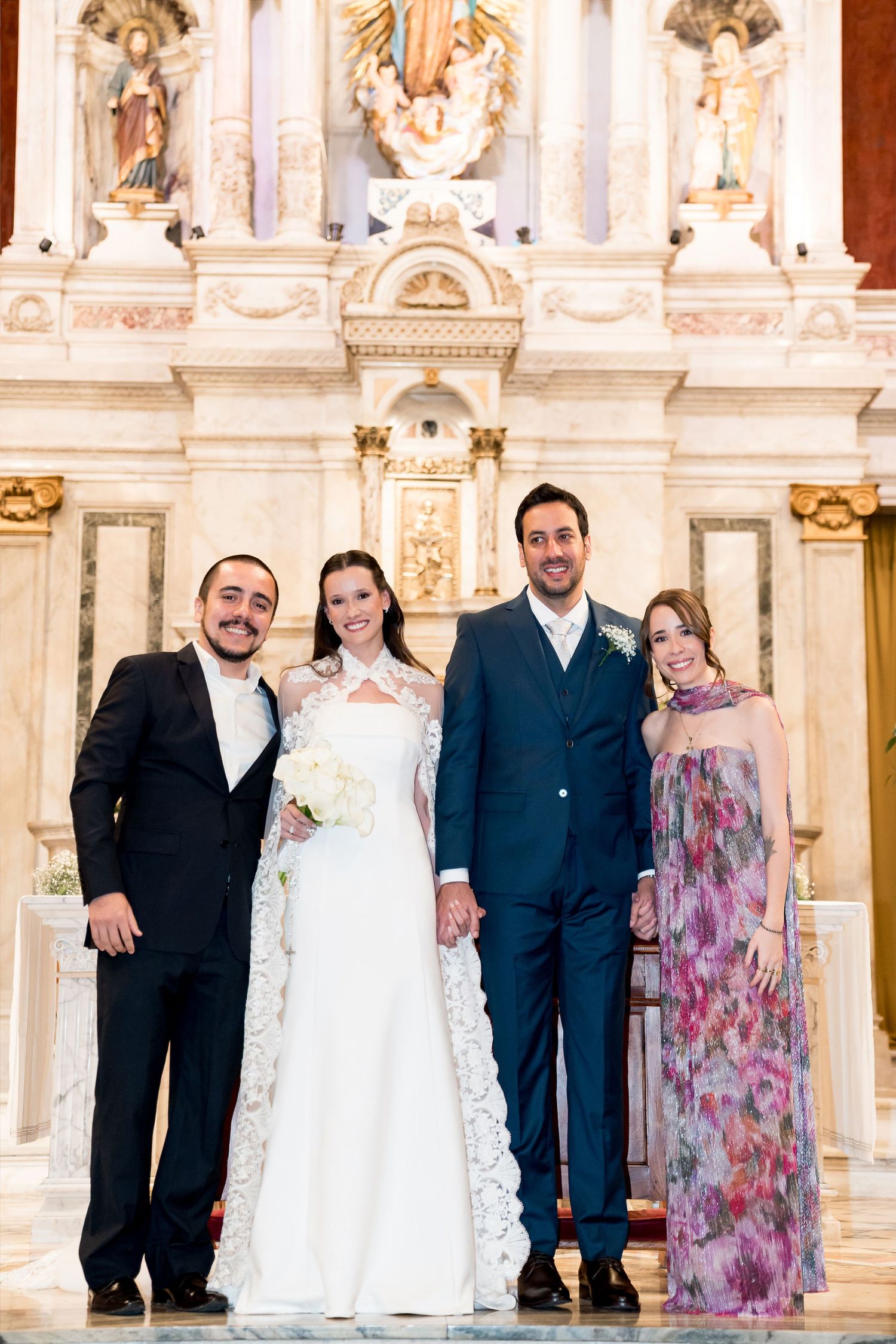 Bride and groom pose with two guests at ornate church altar during wedding ceremony.