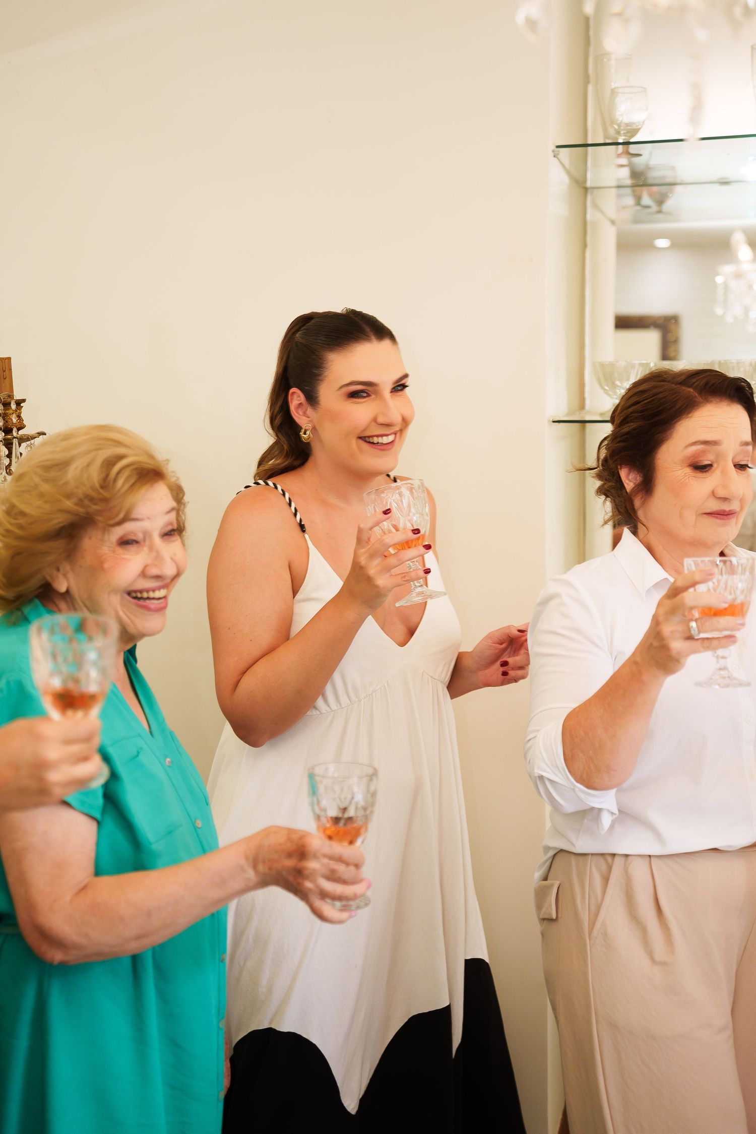 Three women smiling and holding champagne glasses during a celebration, dressed in elegant attire.
