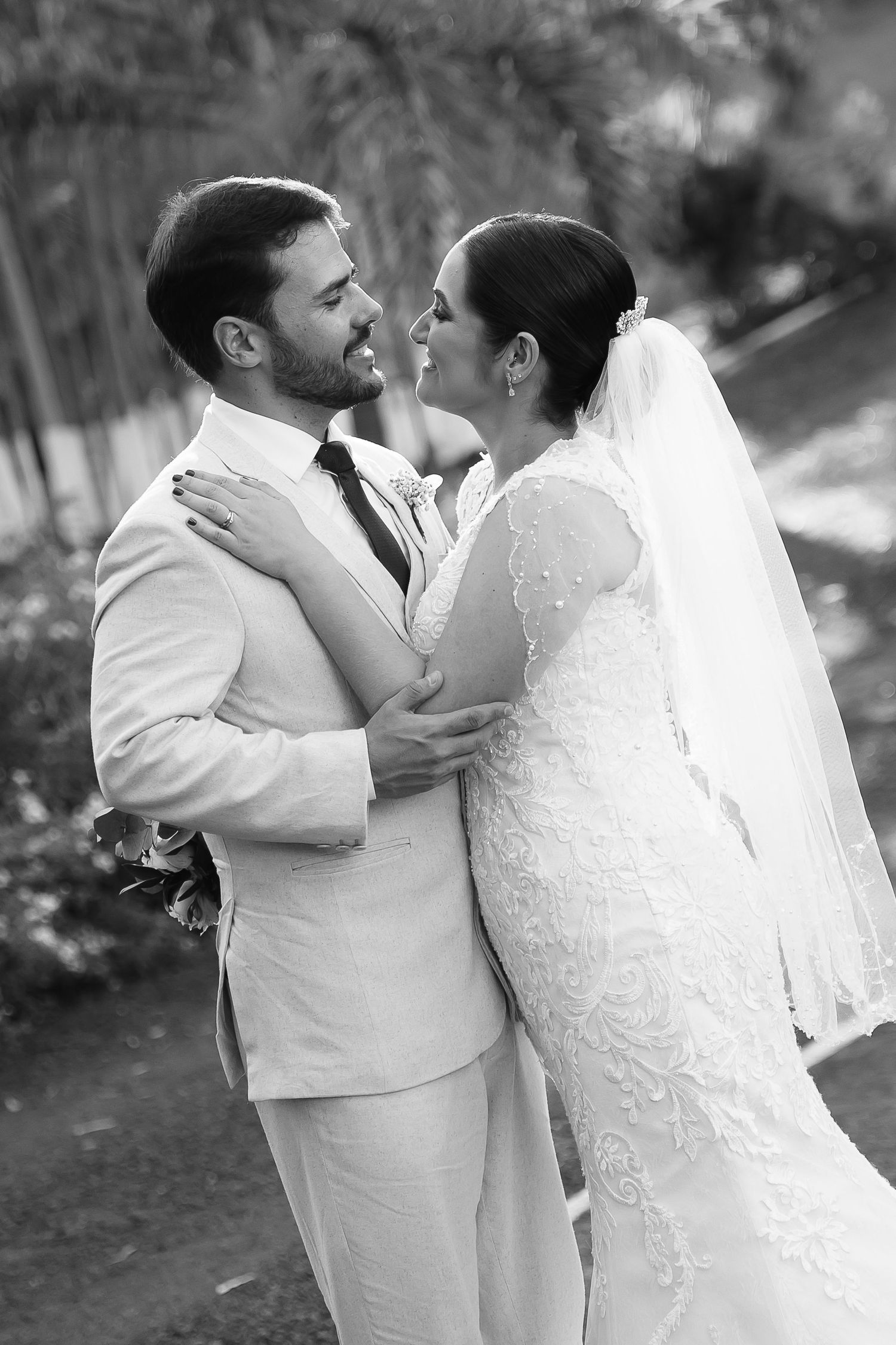 Black and white photo of a bride and groom embracing outdoors, gazing lovingly at each other on their wedding day.