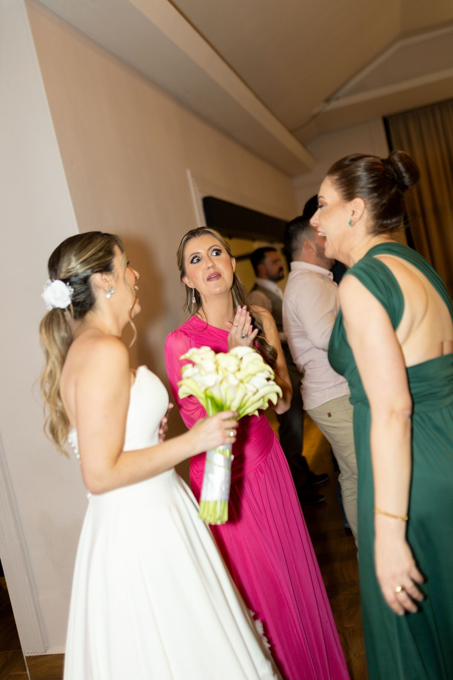 Bride in white gown with bridesmaids in pink and green dresses chatting at a wedding reception.