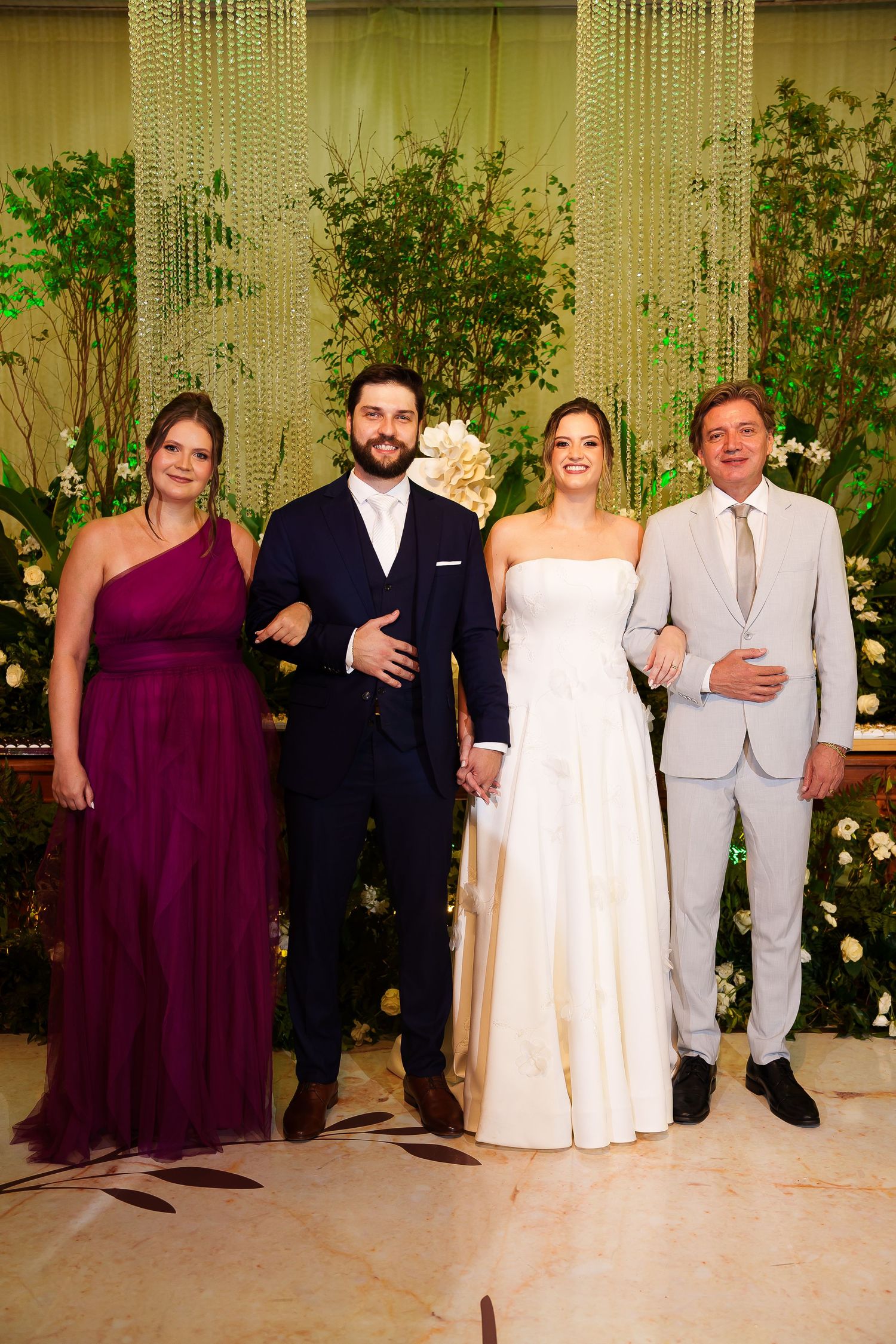 Wedding party of four posing elegantly, bride in white gown, groom in navy suit, guests in purple and grey attire.