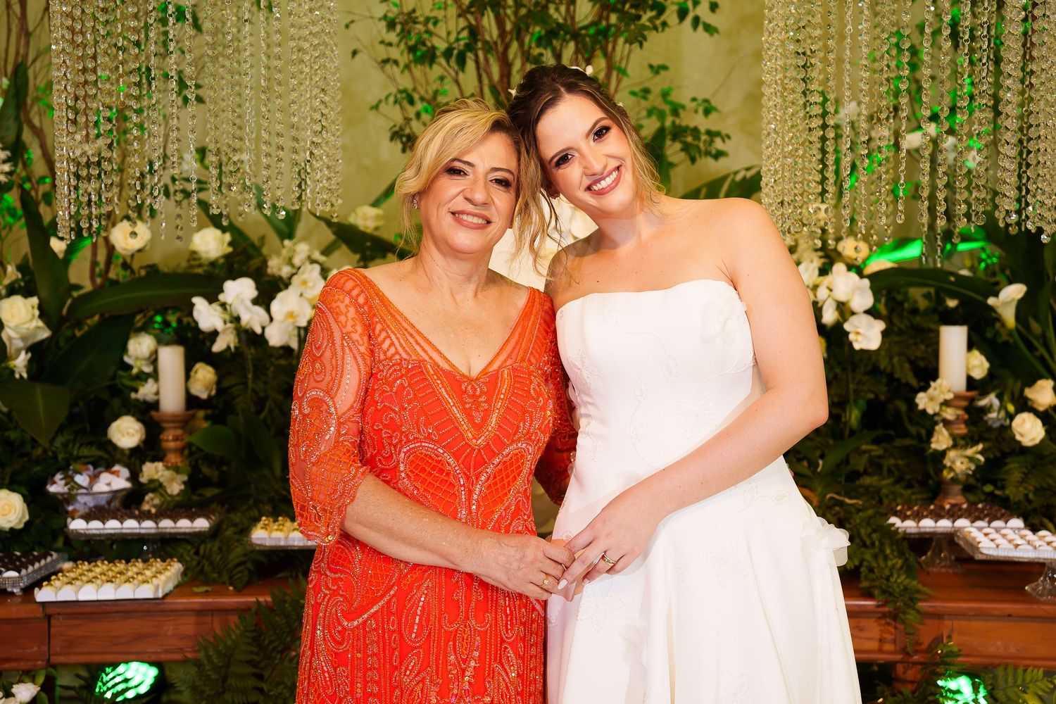 Two women in elegant attire pose together at a wedding reception with floral decor.