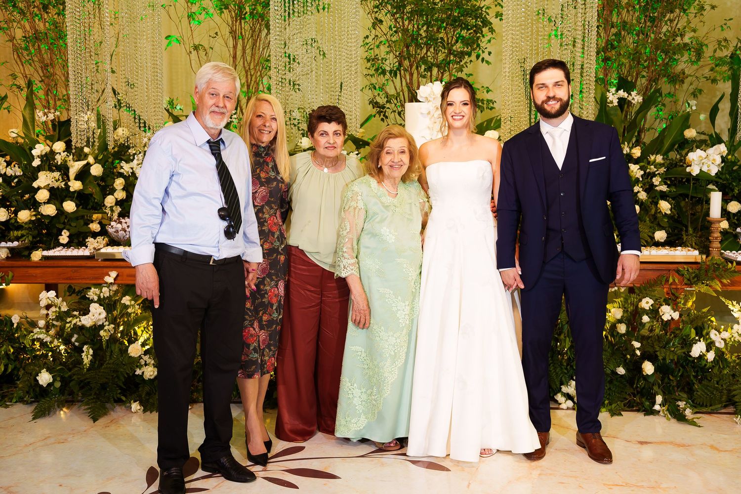 Group of six people posing together at an elegant wedding ceremony surrounded by floral arrangements.