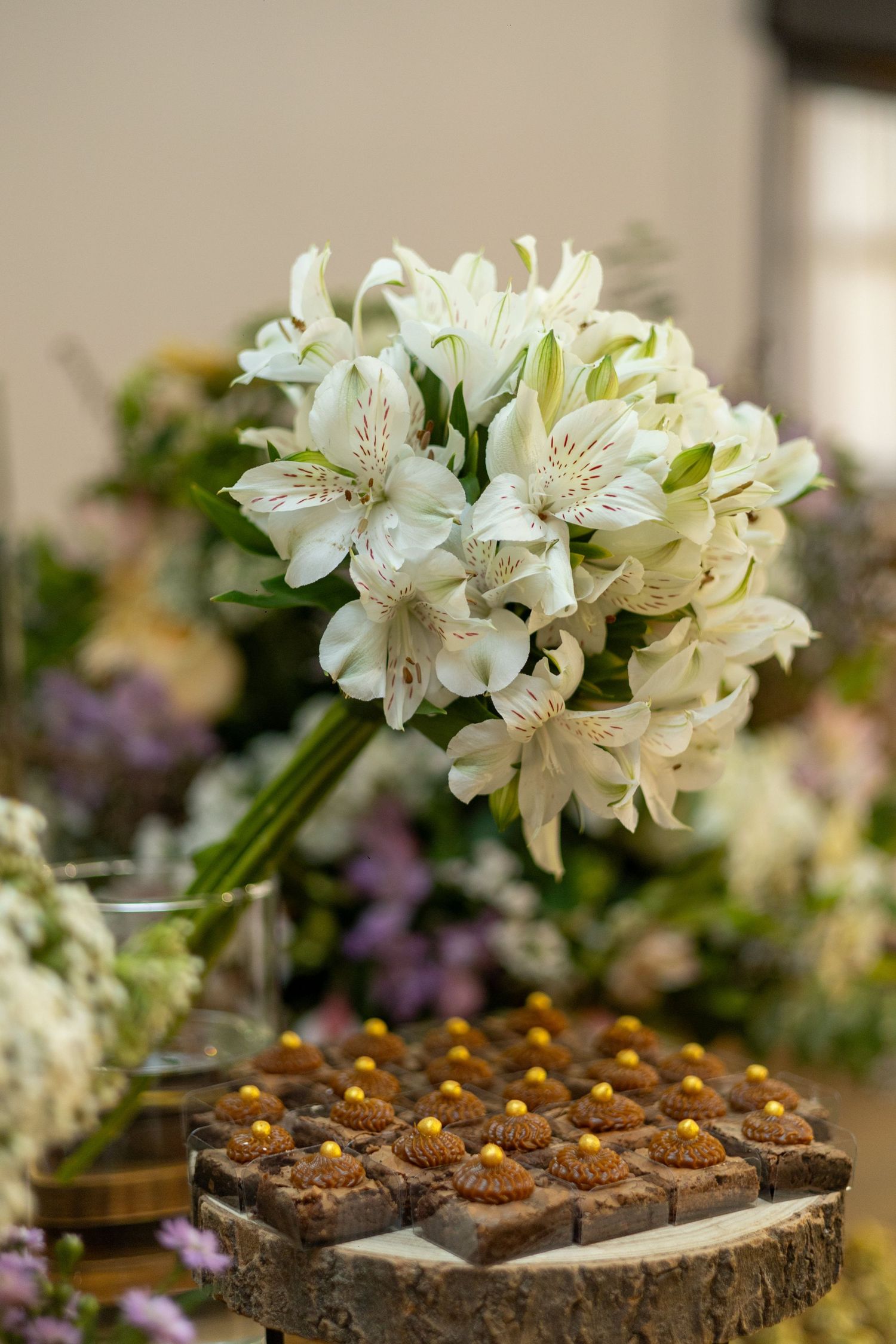 Elegant white alstroemeria bouquet displayed on rustic wood slice with chocolate desserts at a wedding reception.