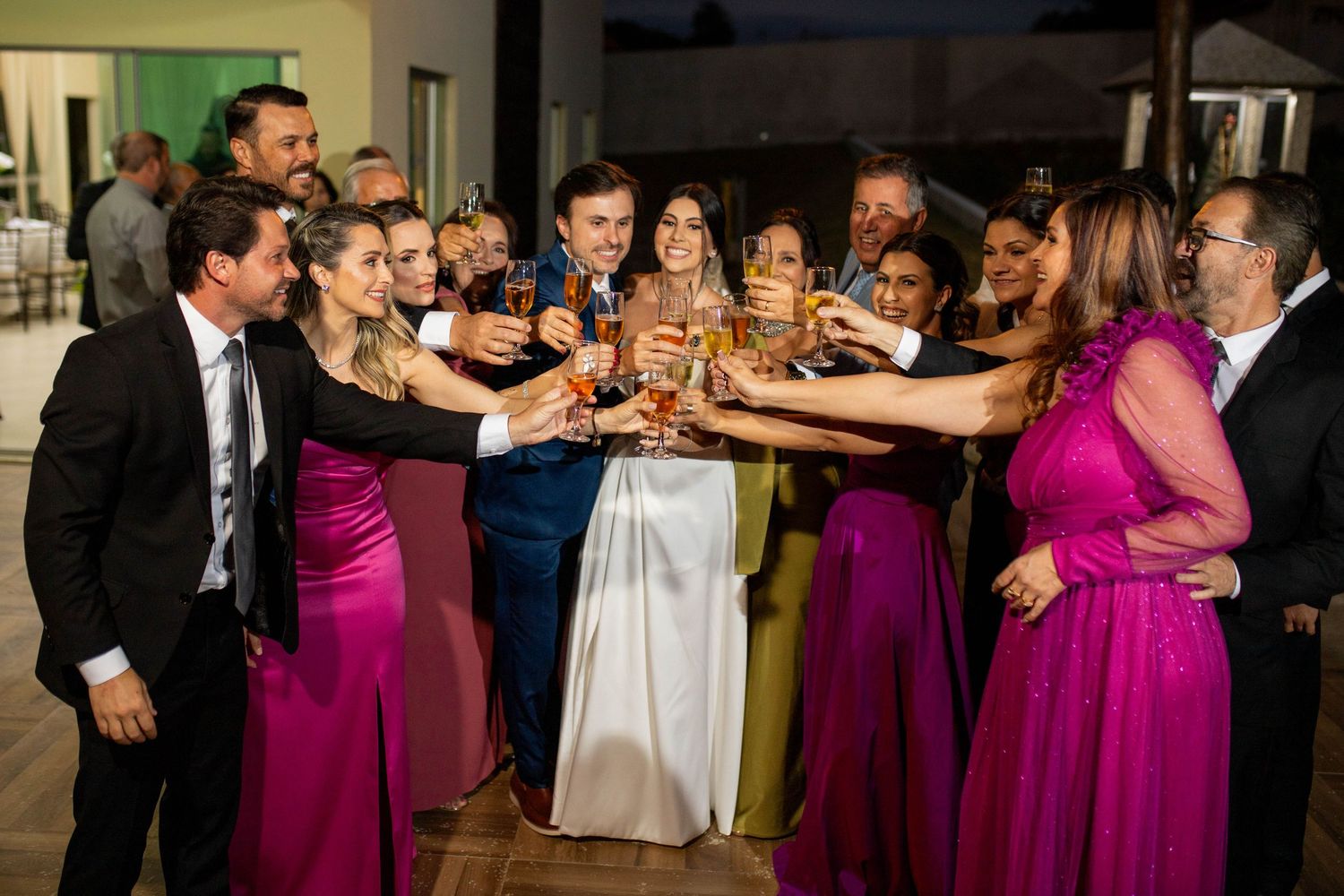 Wedding party in fuchsia dresses and suits toasting with champagne glasses at elegant reception celebration.