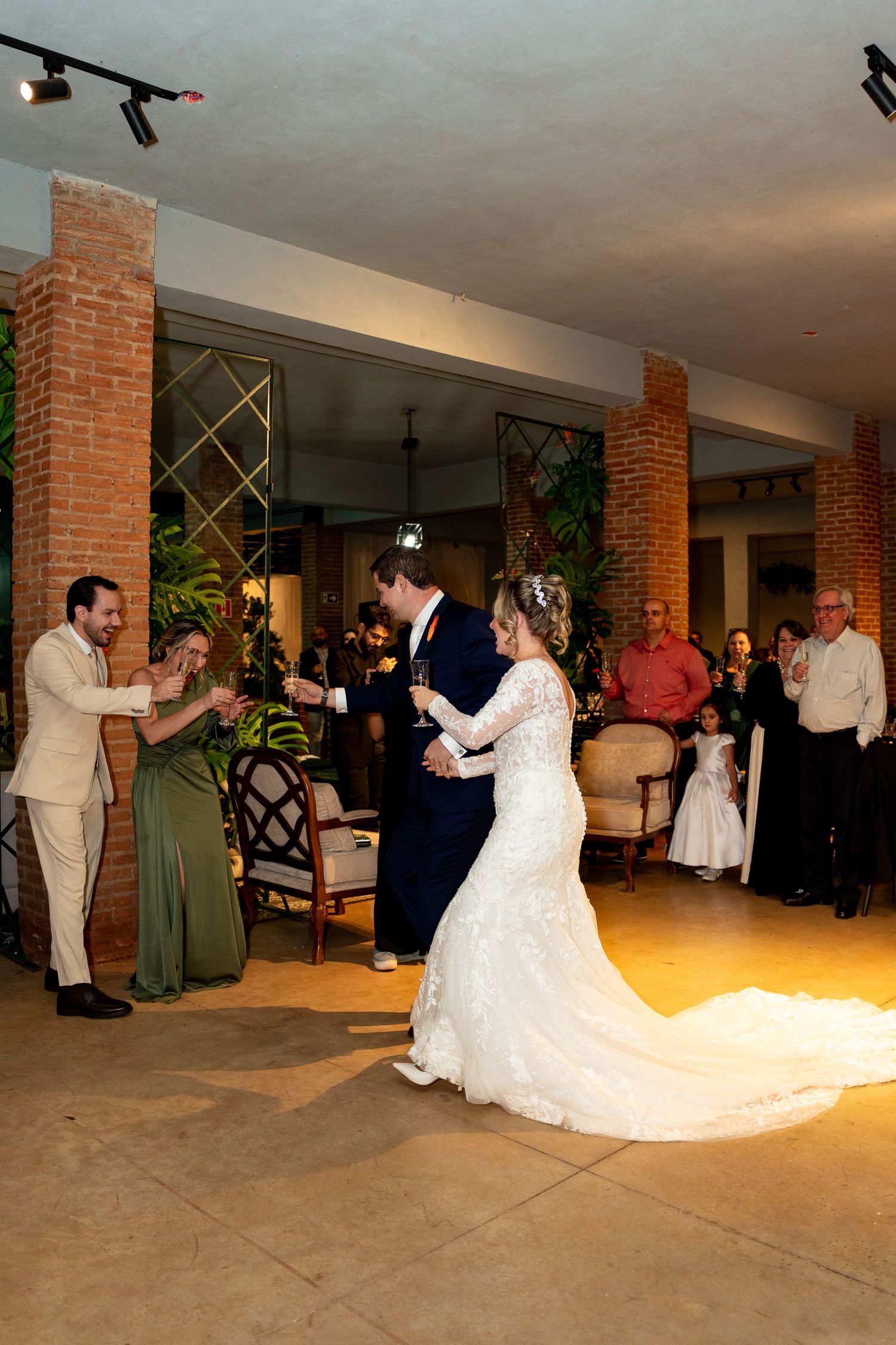 Bride in white lace gown and groom in navy suit share first dance at elegant indoor wedding reception.
