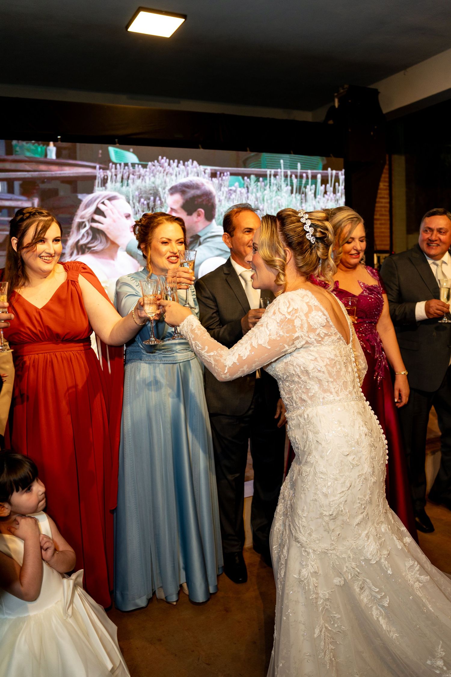 Bride in white lace gown toasting champagne with bridesmaids in colorful gowns at a wedding reception.