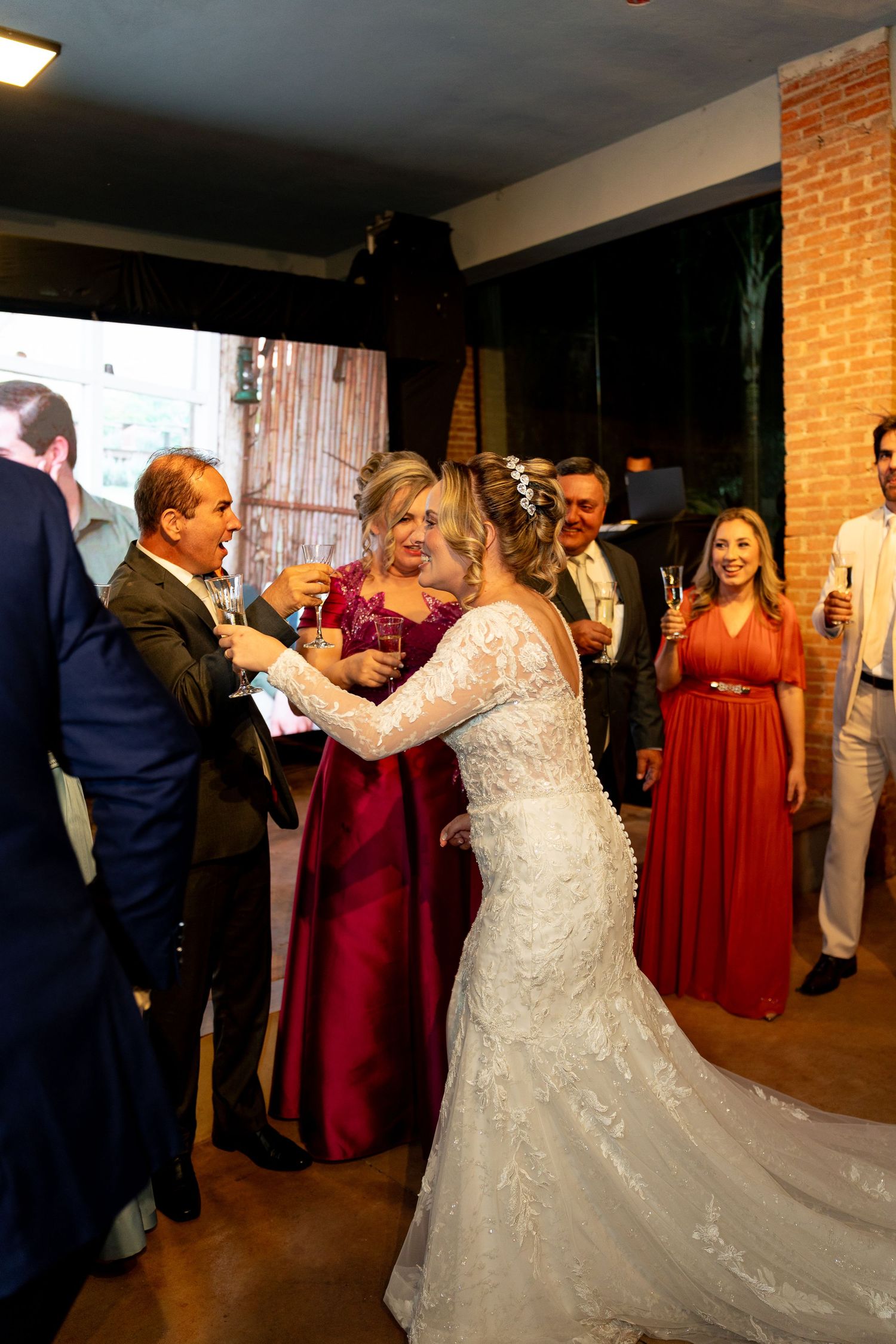 Bride in lace wedding gown dancing with guests at elegant indoor wedding reception celebration.