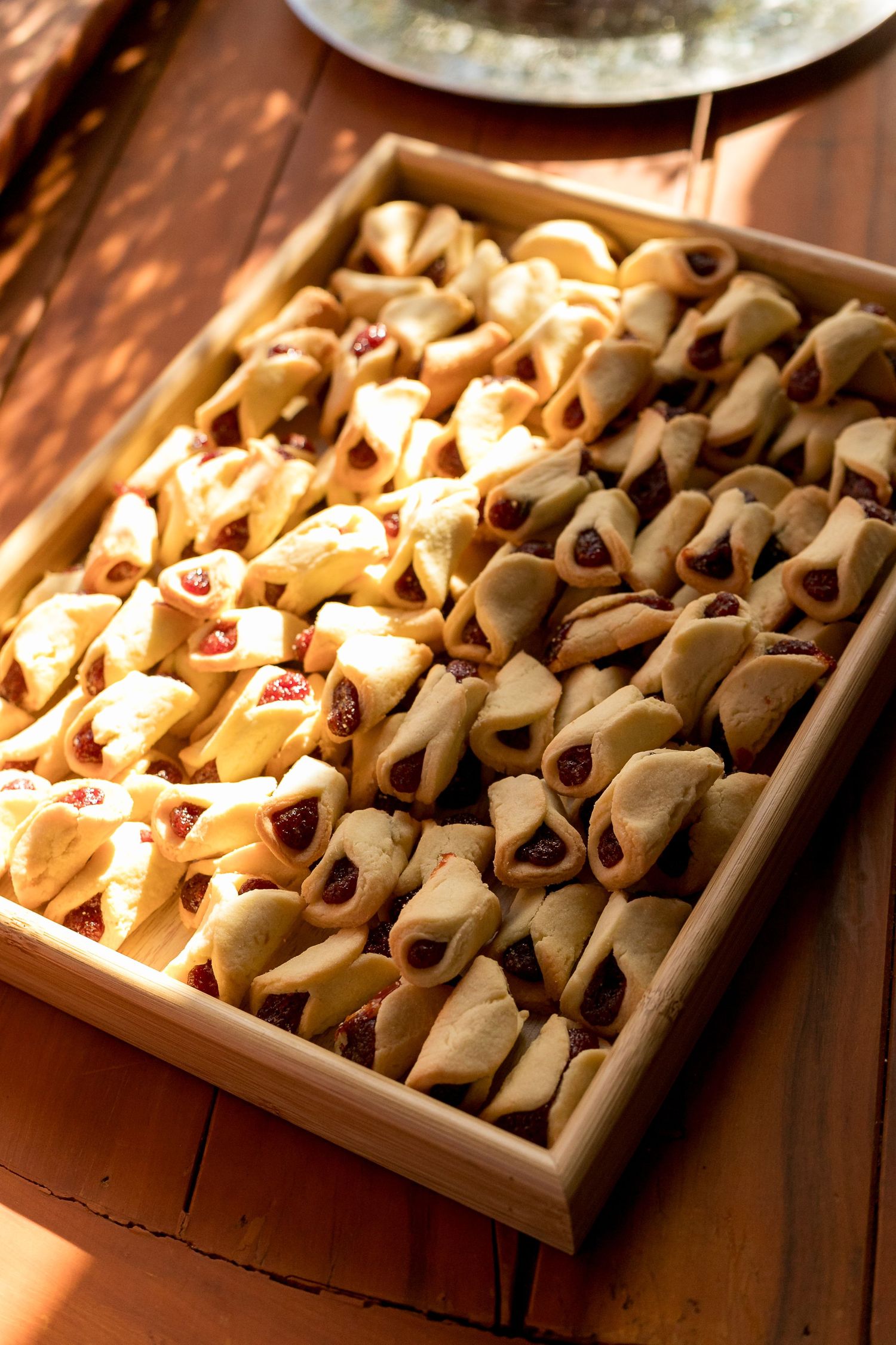 Wooden tray filled with two varieties of hamantaschen cookies, one with red jam and one with chocolate filling.