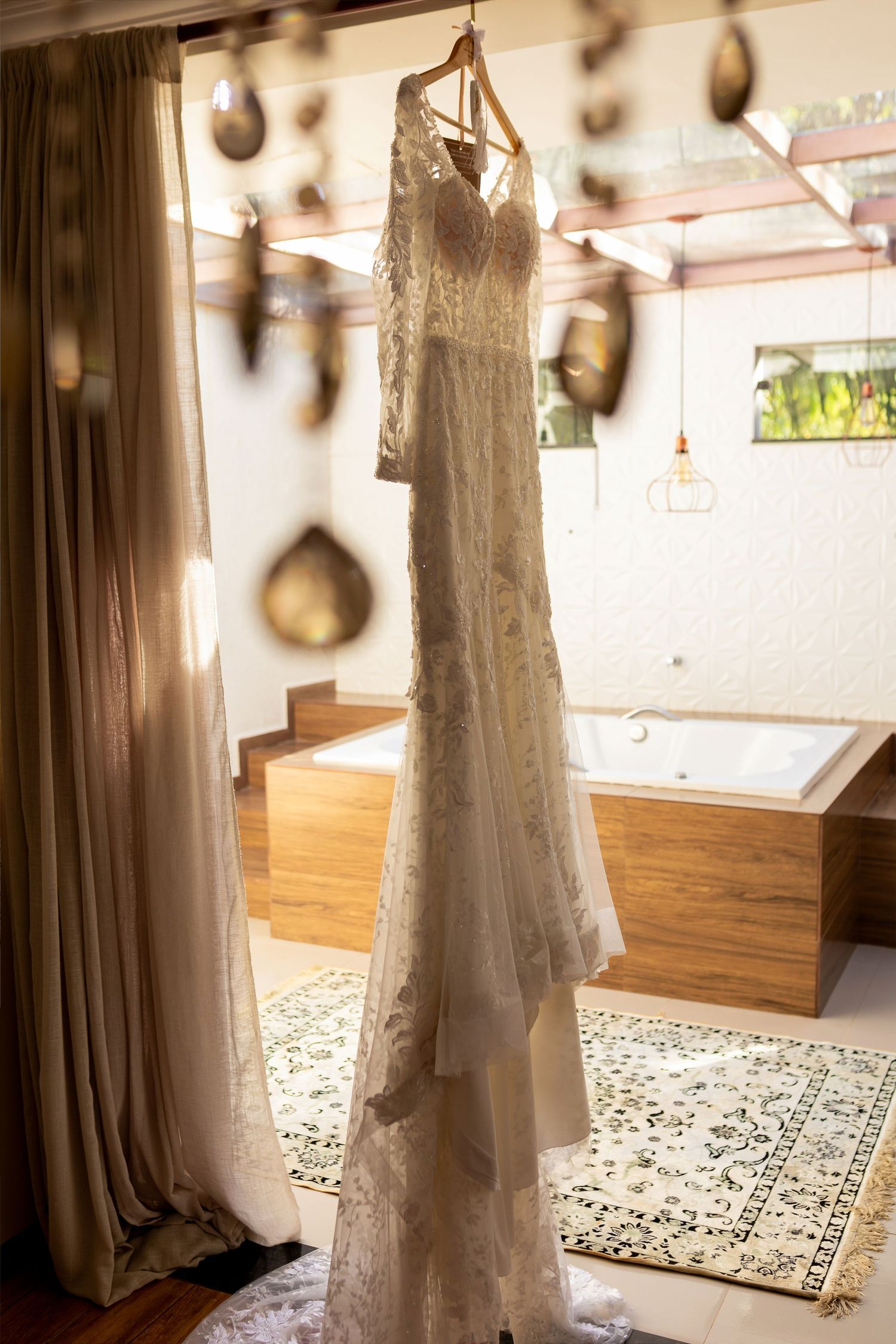 Elegant lace wedding dress hanging on a hanger in a luxurious bridal suite with warm lighting.