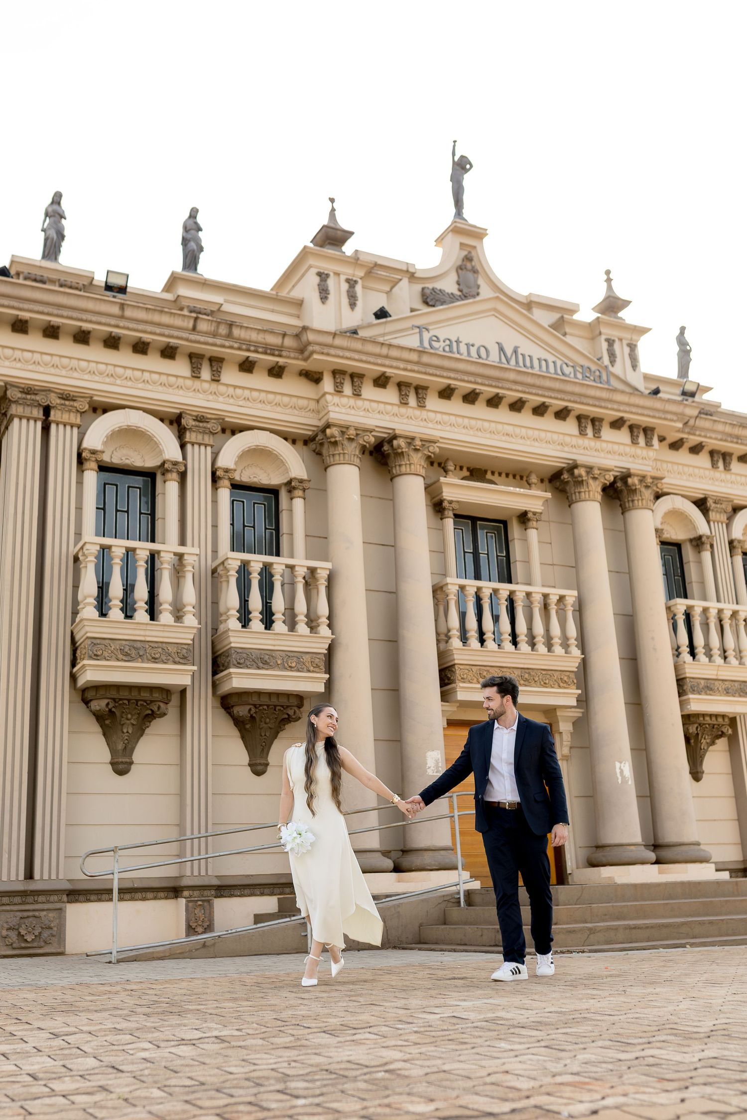 Couple holding hands in front of Teatro Municipal building with classical columns and statues.
