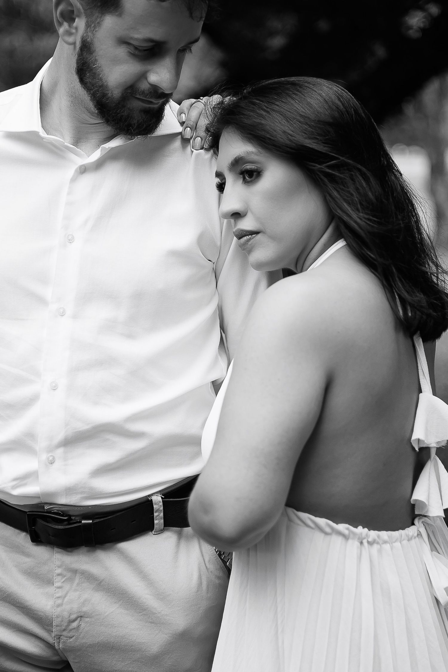 Black and white photo of a romantic couple in white outfits, woman gazing away as man tenderly kisses her hand.