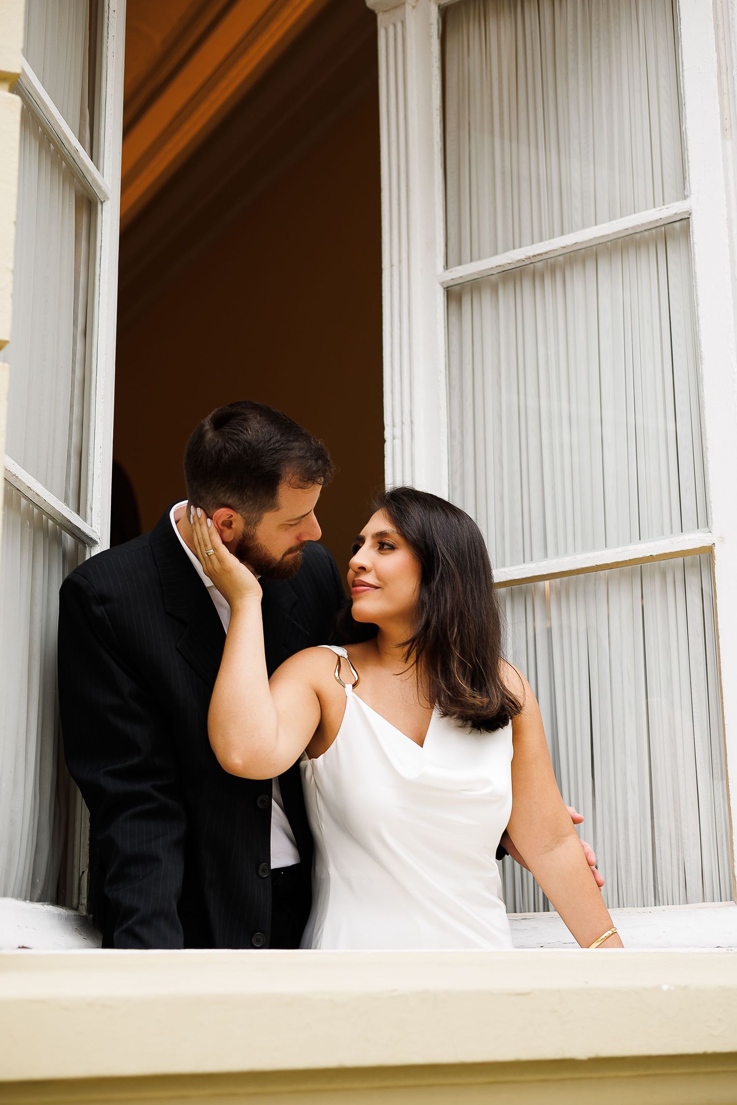 A bride in white dress and groom in black suit share a romantic moment on a building balcony.