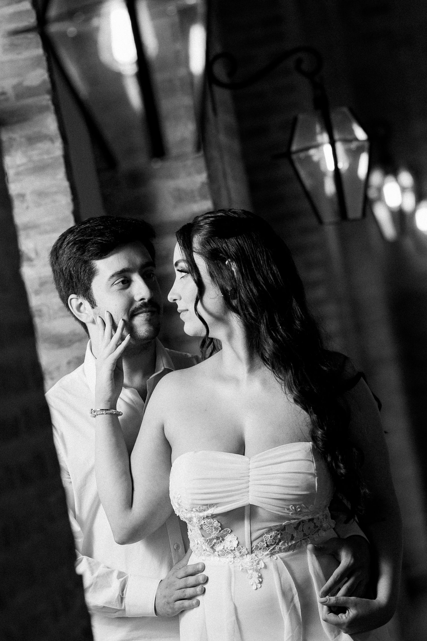 Black and white photo of a romantic couple in wedding attire gazing at each other near decorative lanterns.