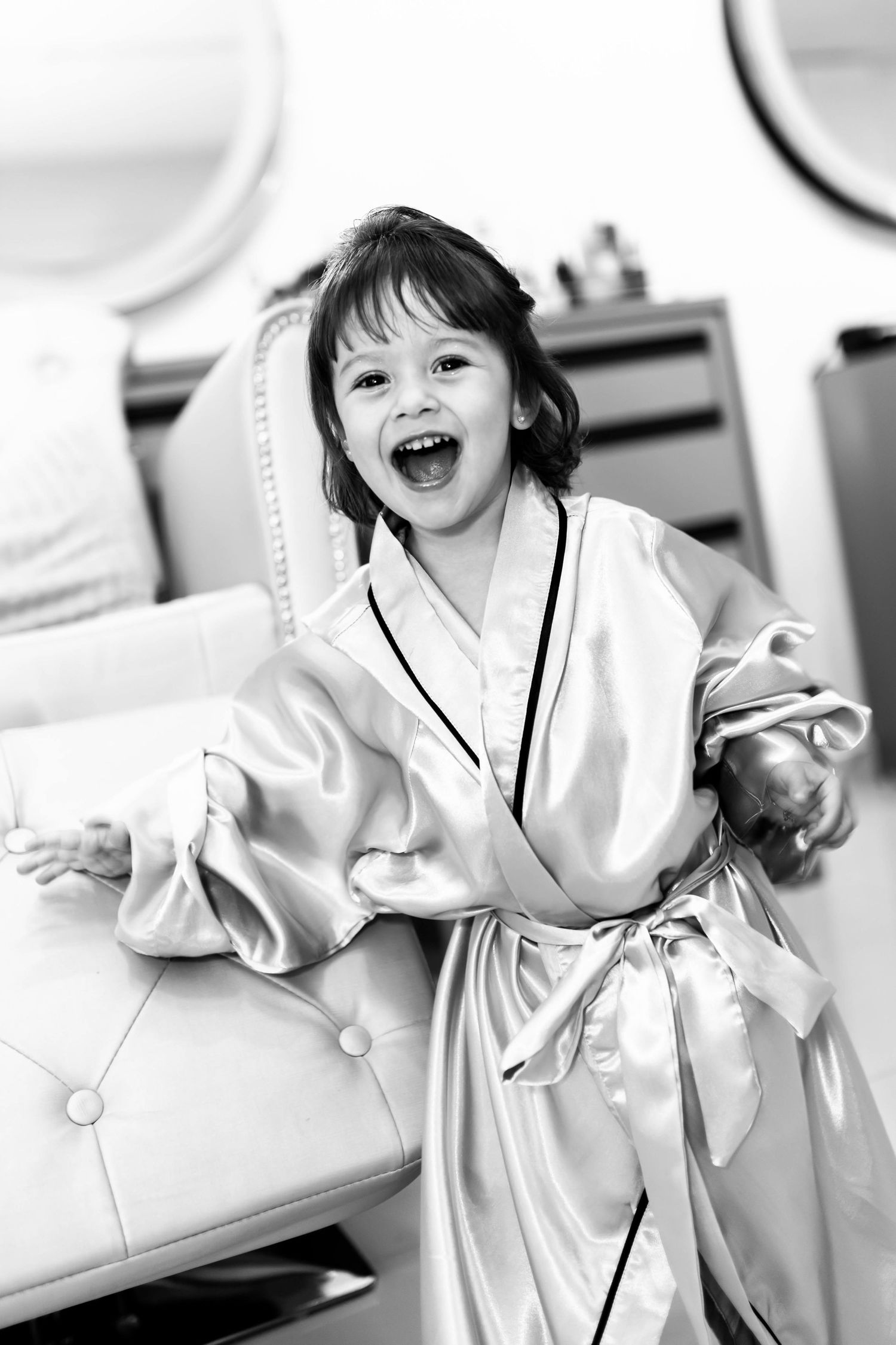 Joyful young girl laughing in a satin robe, black and white portrait photo.