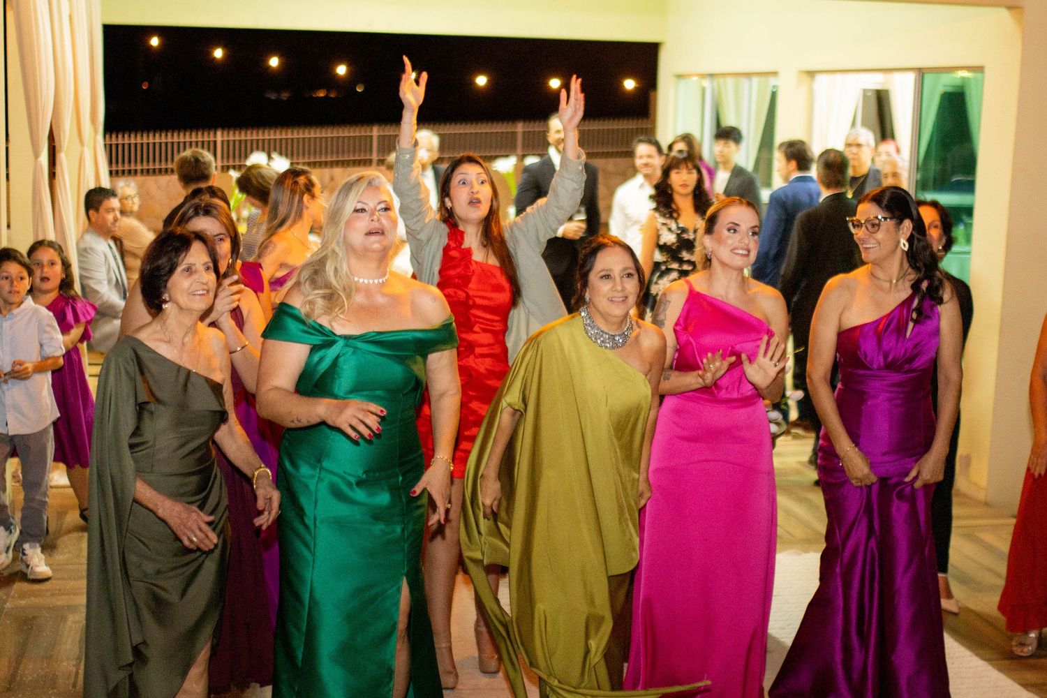Colorful group of women in elegant gowns celebrating at a festive evening party with sparklers.
