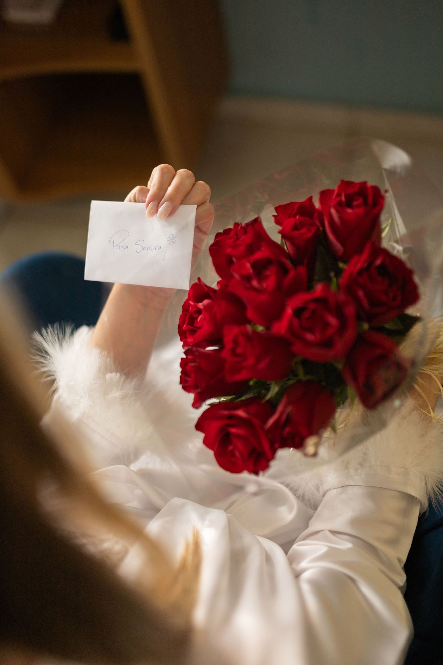 Woman in white robe holding a card with a bouquet of red roses in her lap.