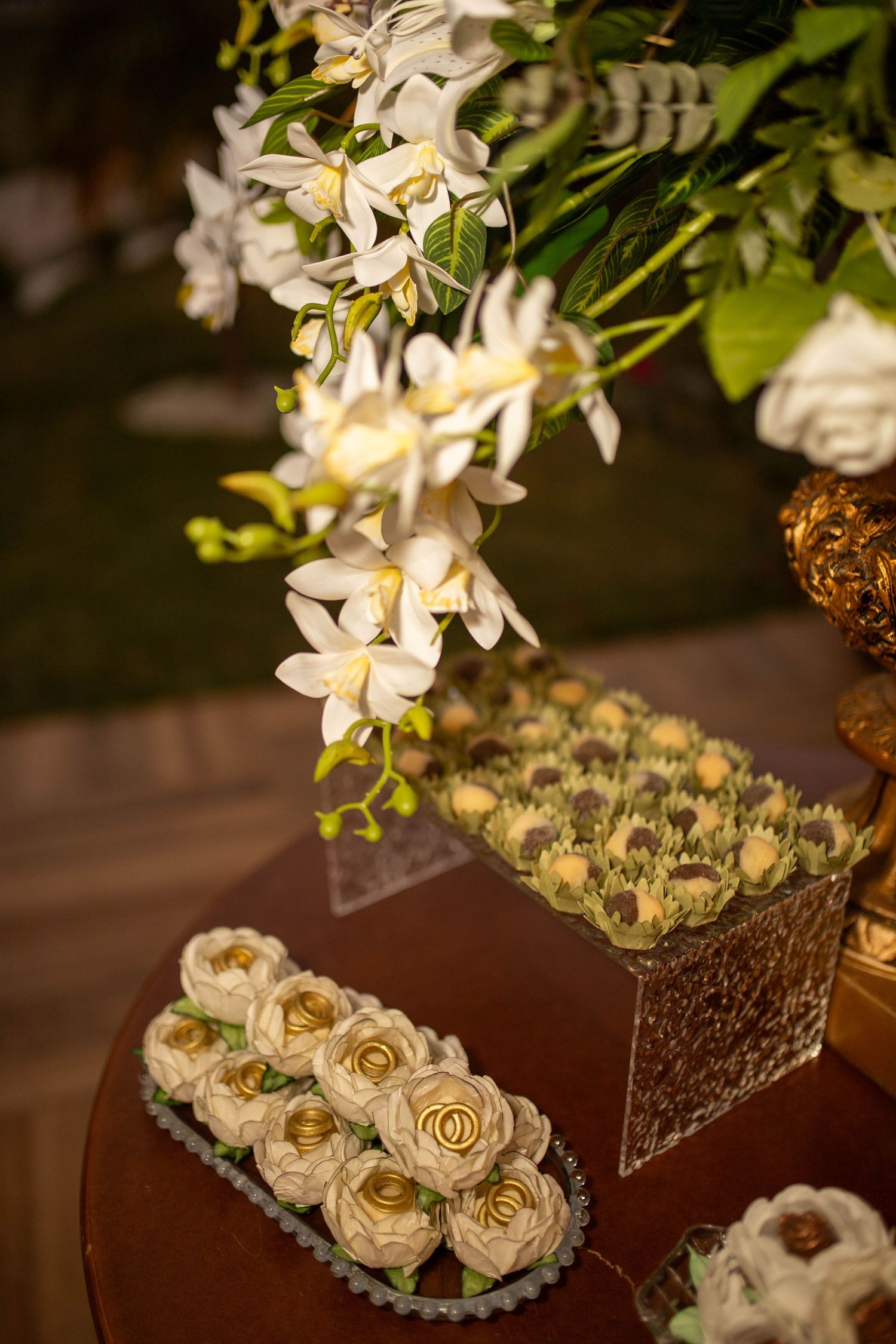 Elegant wedding dessert table with white rose cupcakes, gold accents, and cascading white orchid floral arrangements.