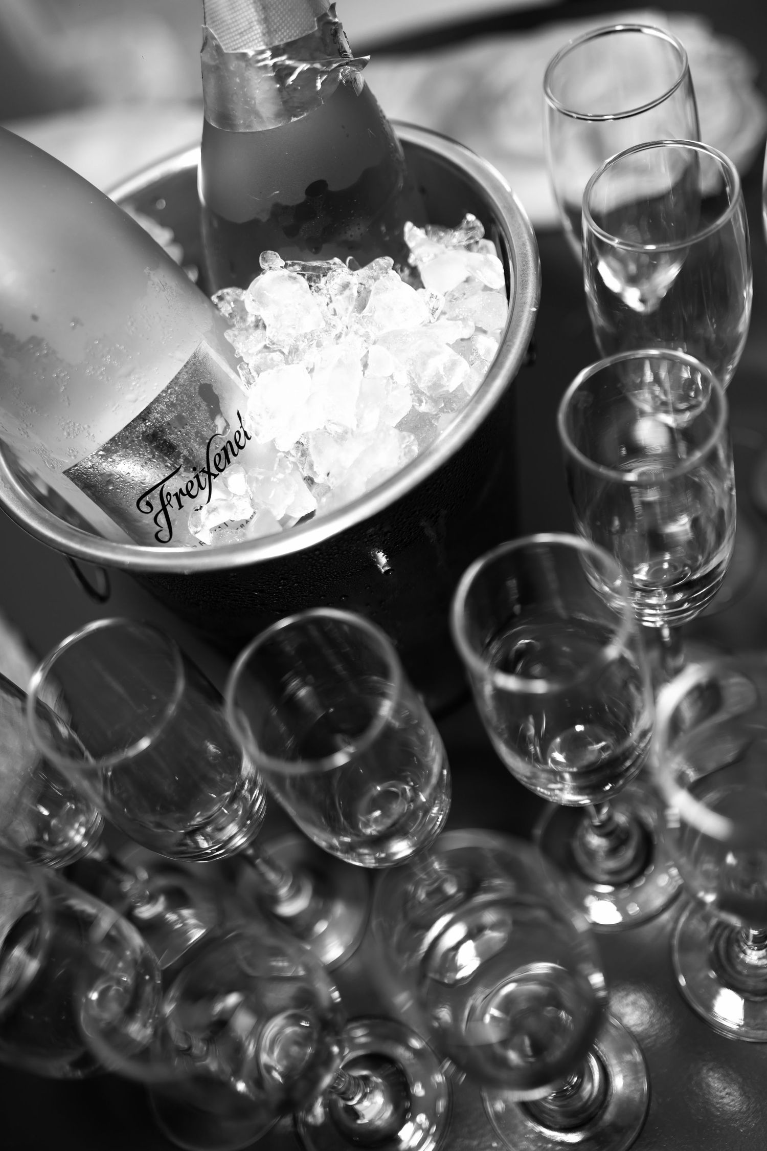Black and white photo of Freixenet champagne chilling in ice bucket surrounded by empty champagne flutes.