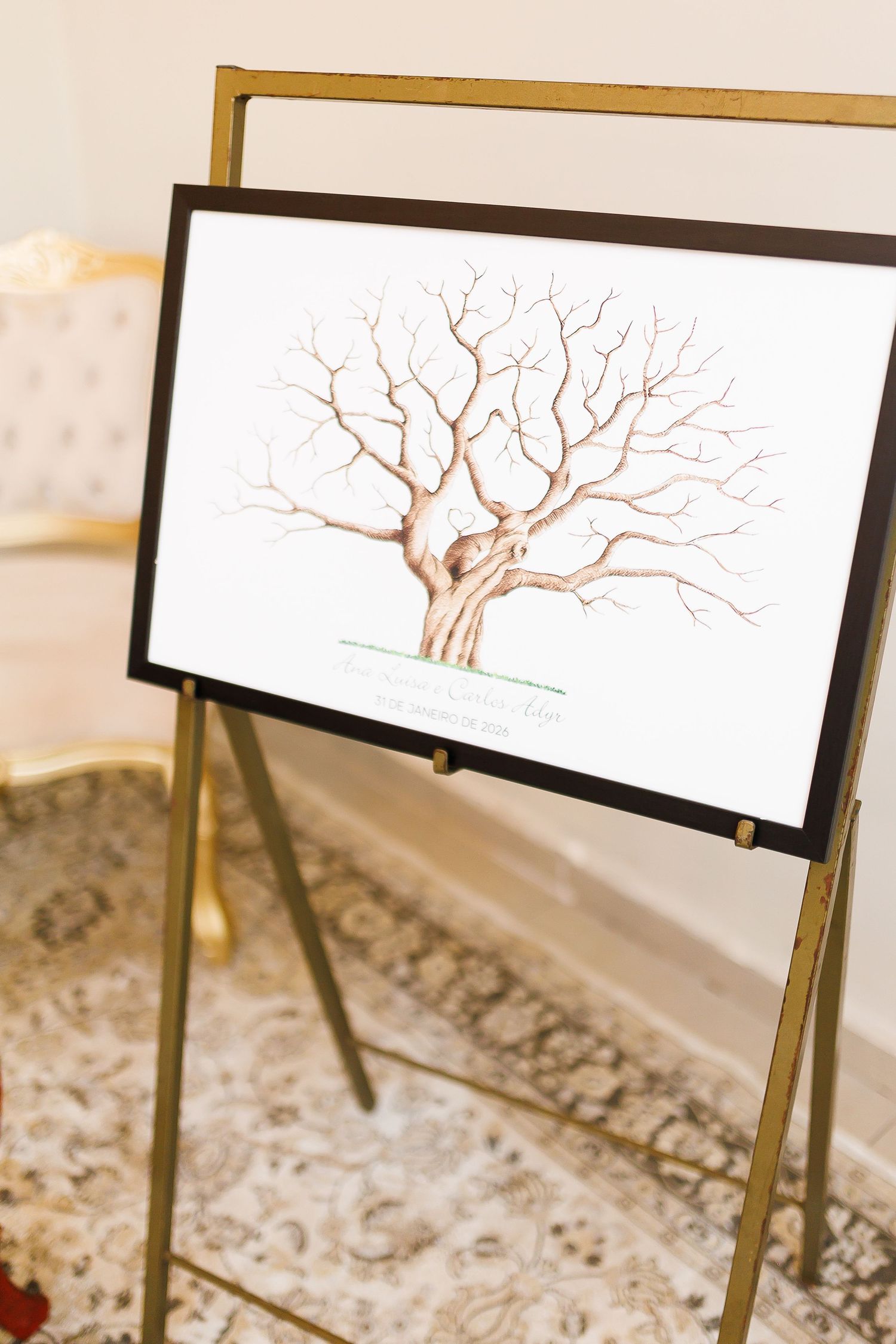 Framed fingerprint tree wedding guest book art displayed on a gold easel stand in an elegant white room.