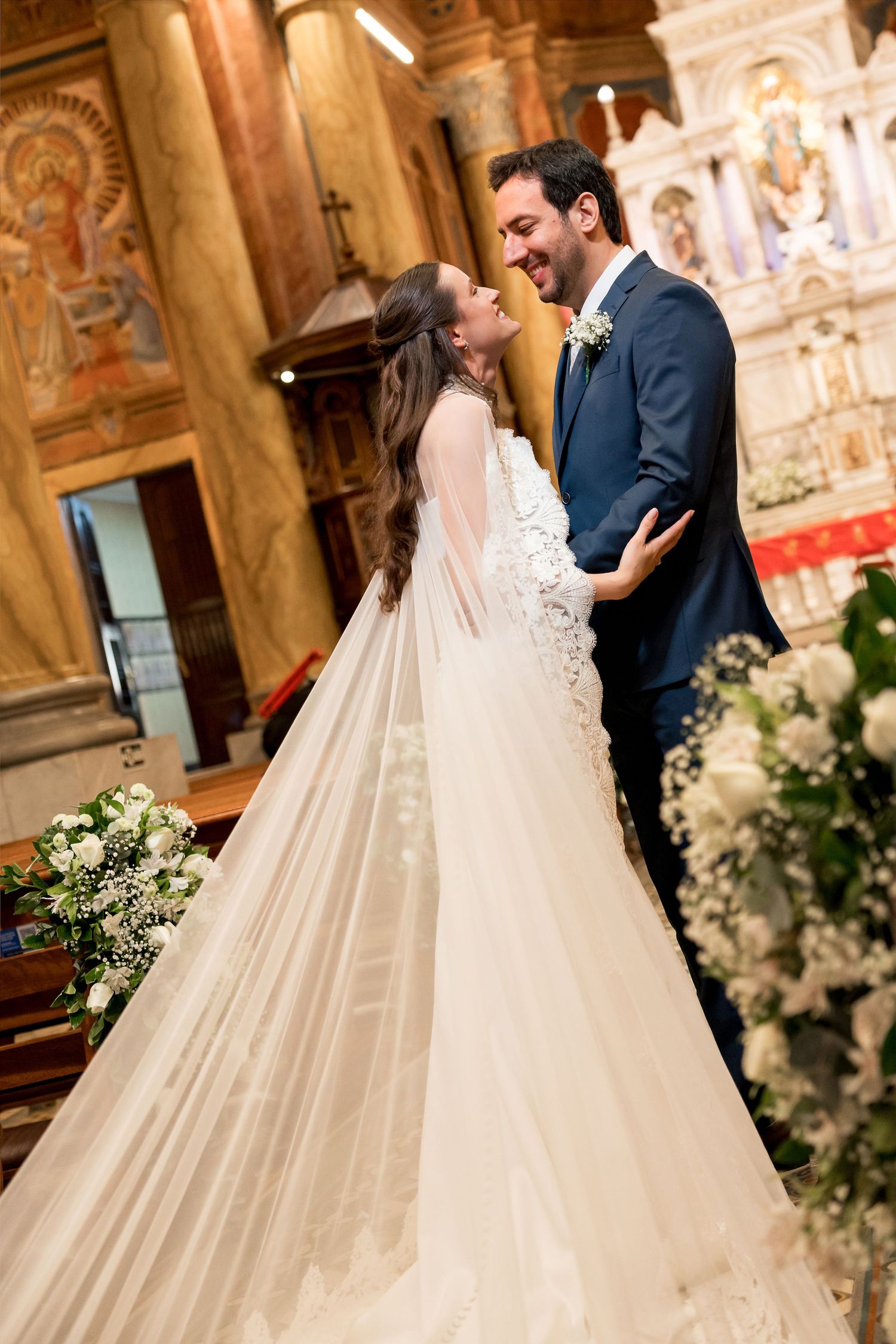Bride and groom share a joyful moment at the church altar, with her elegant white gown and veil trailing behind.