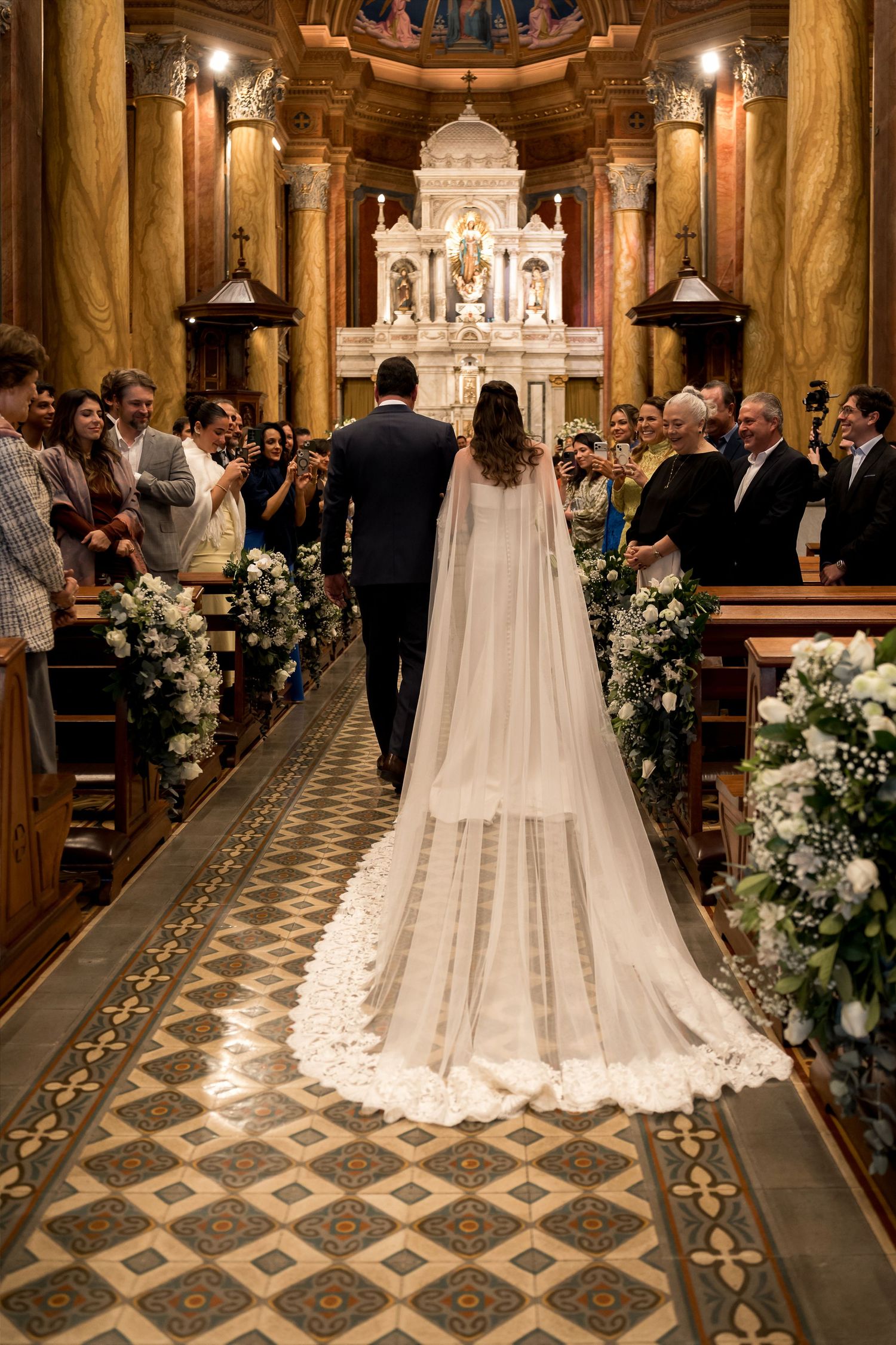 Bride and groom walking down the aisle of an ornate church, bride wearing a long lace cape veil.