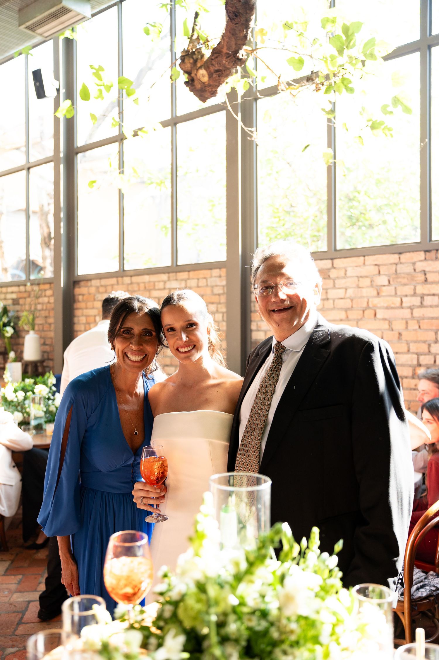 Bride in white gown poses with guests in blue dress and dark suit at elegant wedding reception.
