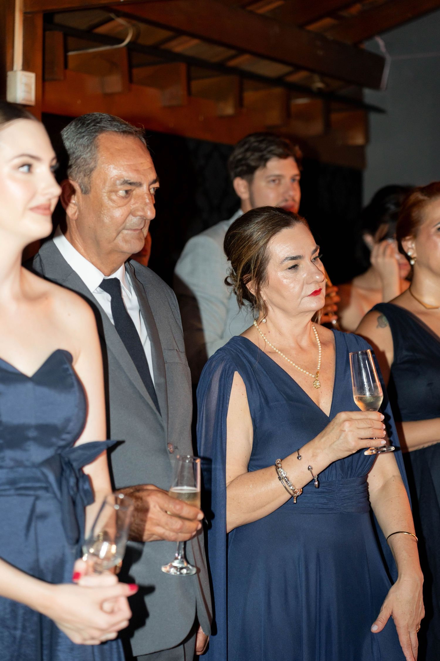 Elegantly dressed guests in navy blue attire holding champagne glasses at a formal evening event.